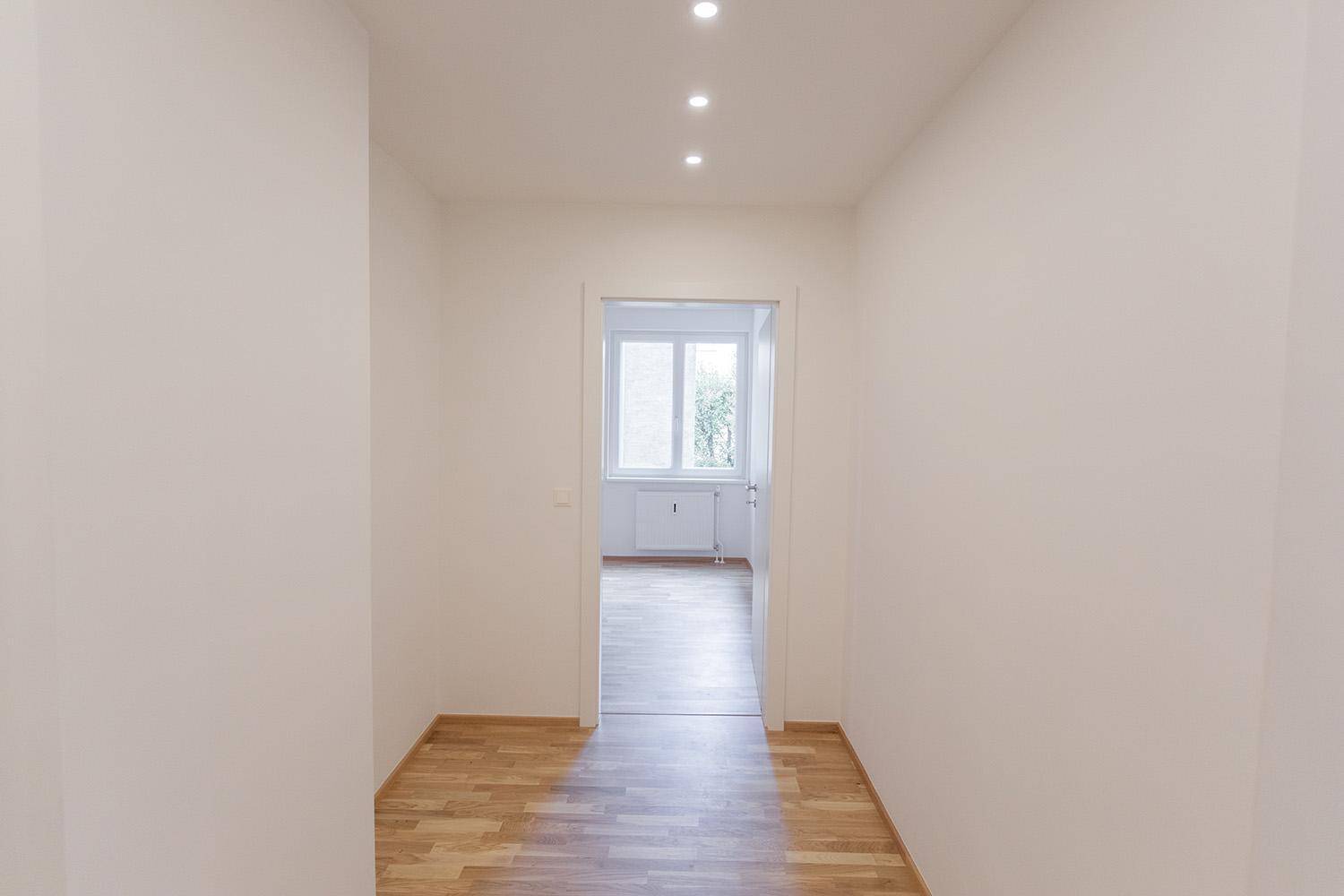 Heller Flur mit Holzboden und Blick in ein weiteres Zimmer mit Fenster.