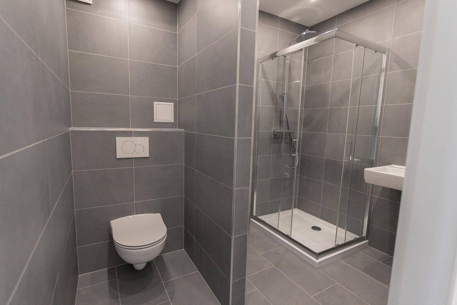 Modernes Badezimmer mit grauen Fliesen, einer Duschkabine und einem wandhängenden WC.