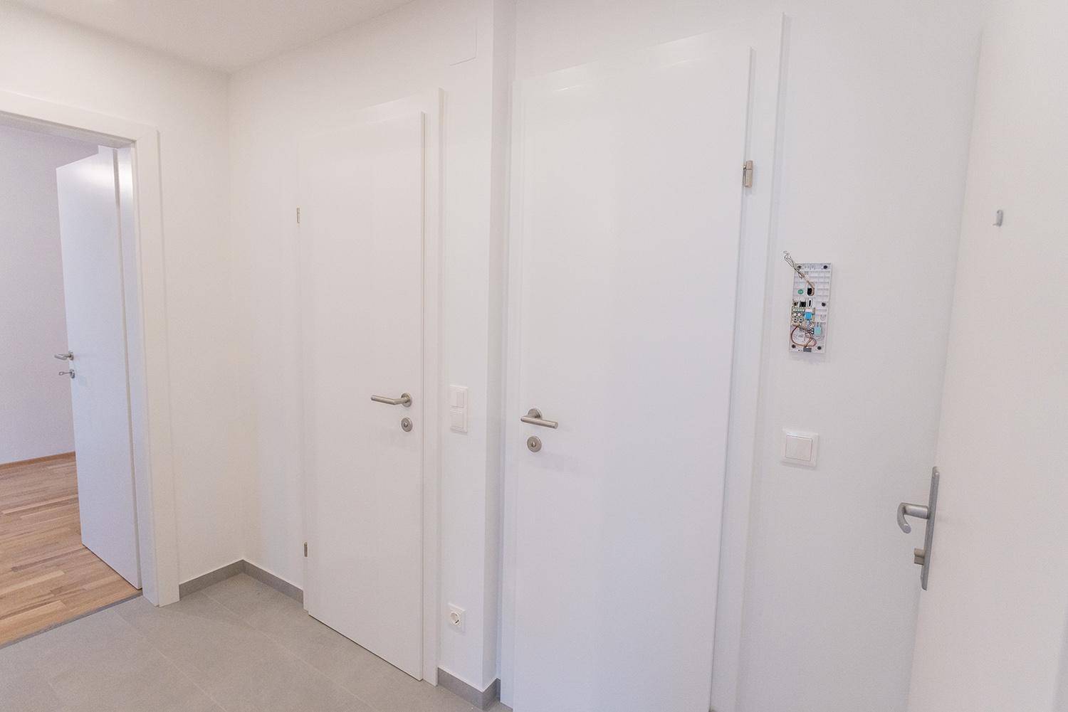 Geräumiger Flur mit hellen Wänden und Türen, der zu weiteren Zimmern mit Parkettboden führt.