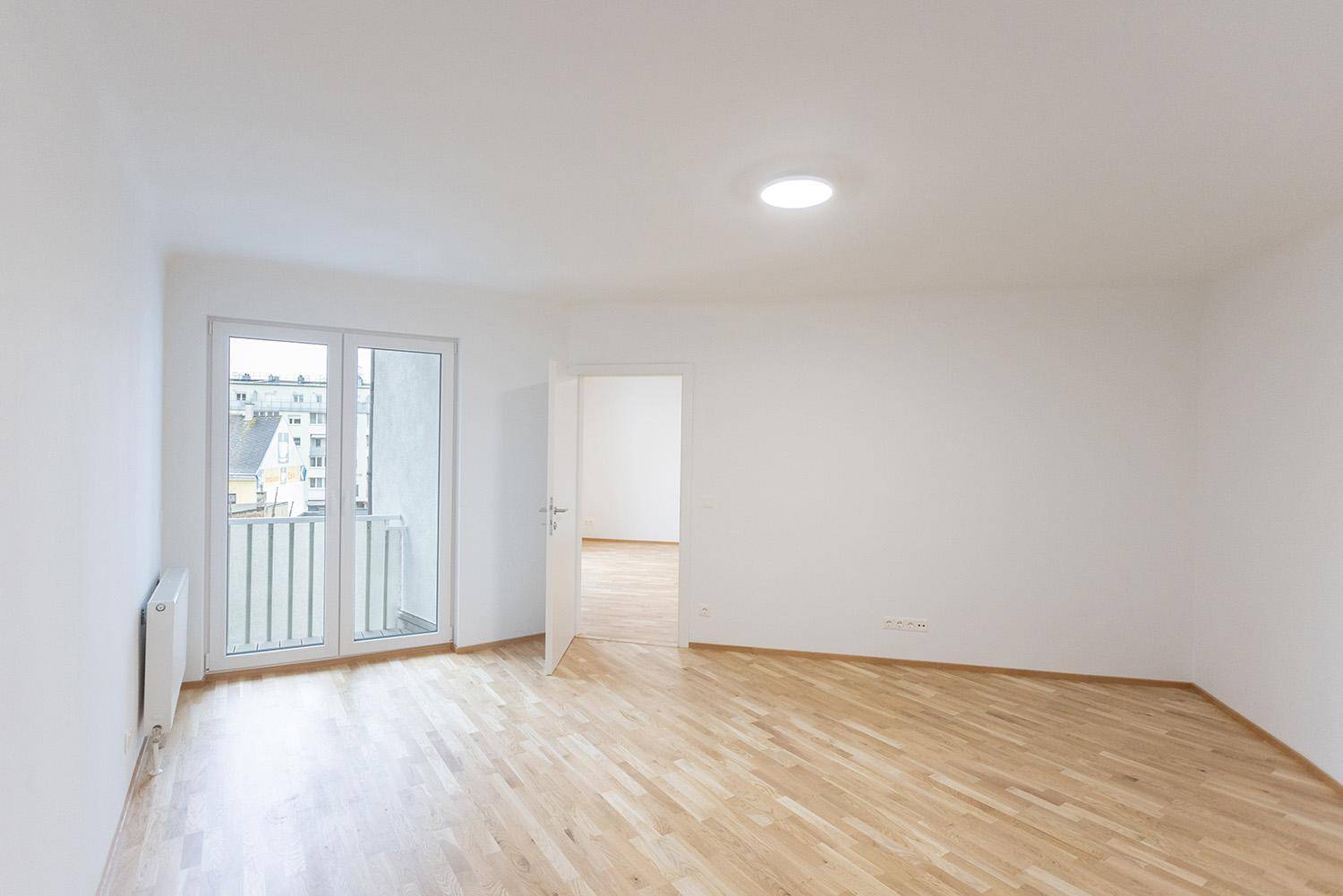 Geräumiger, heller Wohnbereich mit Holzboden und Zugang zu einem französischen Balkon.