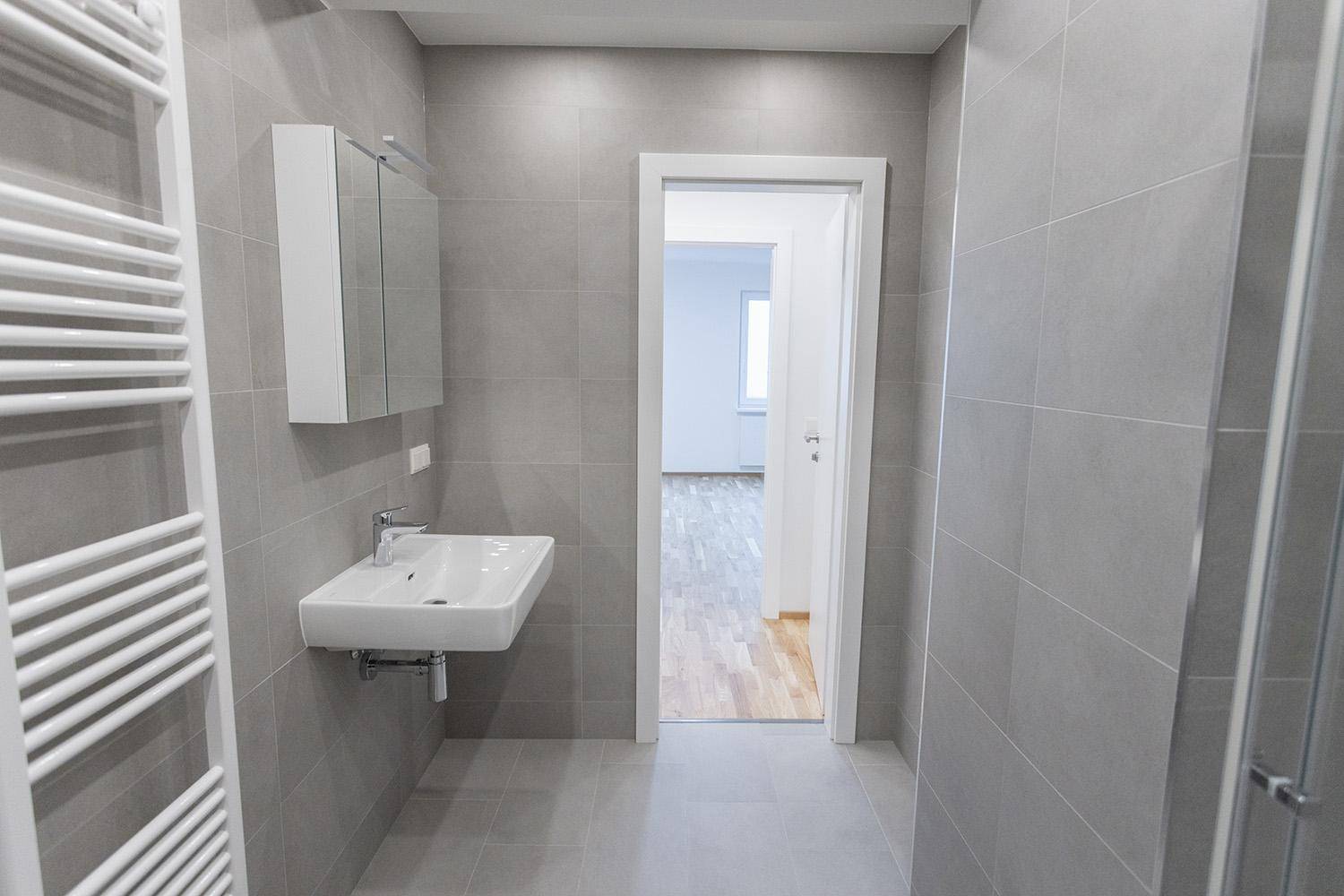 Helles Badezimmer mit Waschbecken, Spiegelschrank und Zugang zu einem angrenzenden Zimmer.