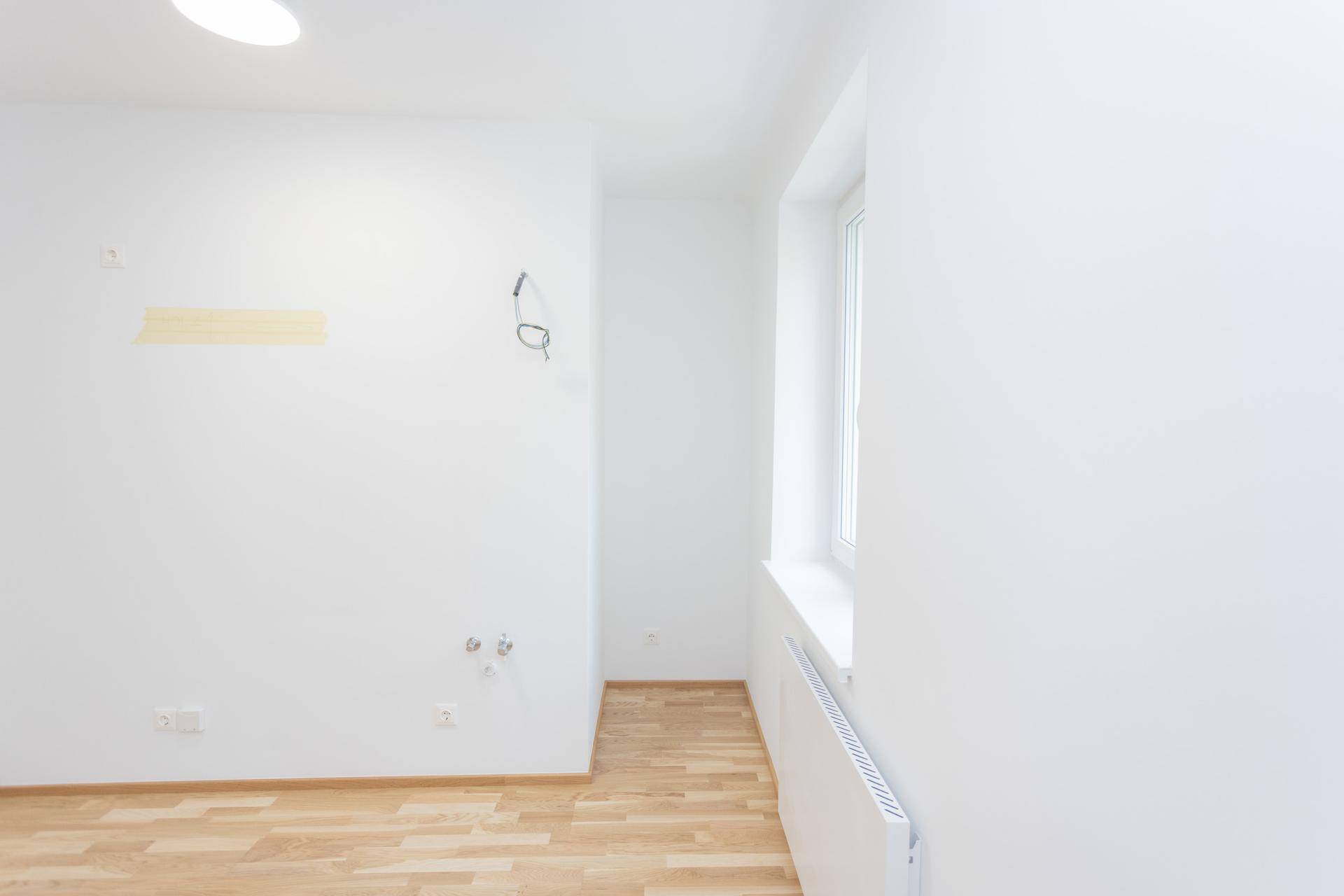 Heller Raum mit Parkettboden und vorbereiteten Anschlüssen für eine zukünftige Küche.