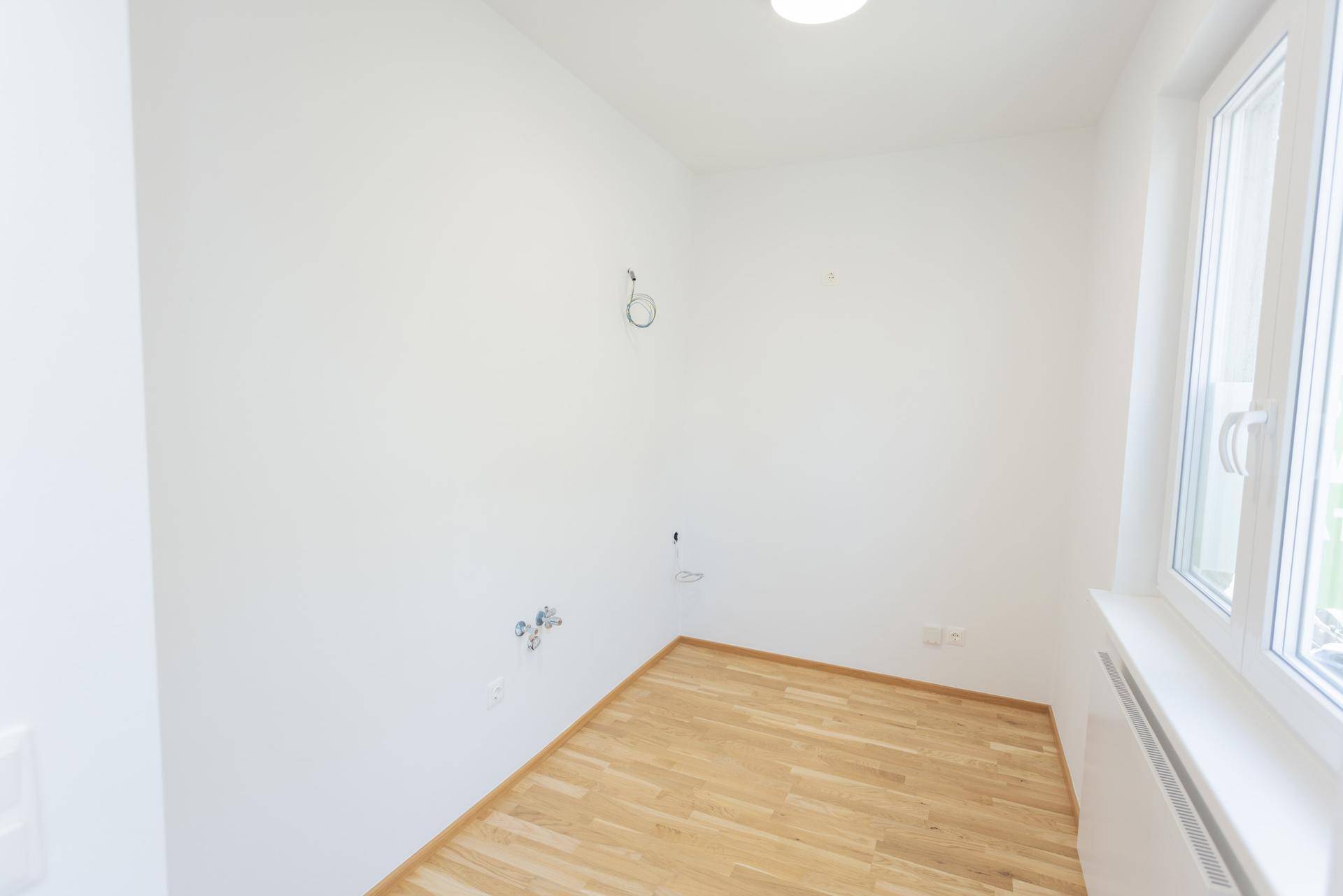 Leerer Küchenraum mit Parkettboden und Fenster, vorbereitet für die Installation einer Einbauküche.