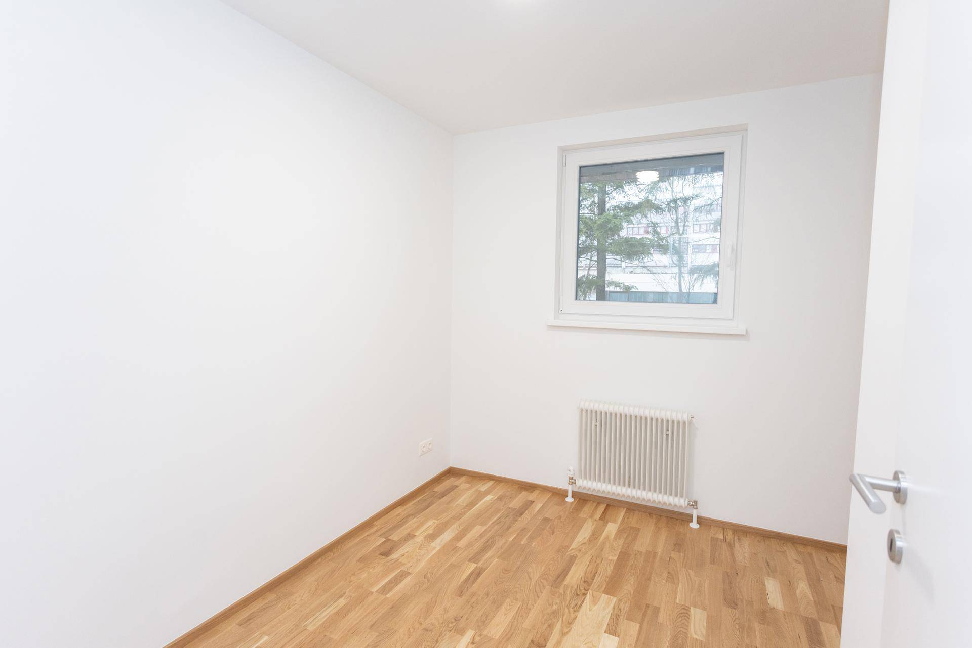 Heller, leerer Raum mit Parkettboden und Fenster, ideal als Kinder- oder Arbeitszimmer.