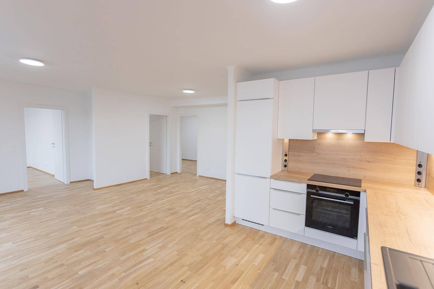 Moderne Einbauküche mit weißen Schränken, Holz-Arbeitsplatte und integriertem Backofen.