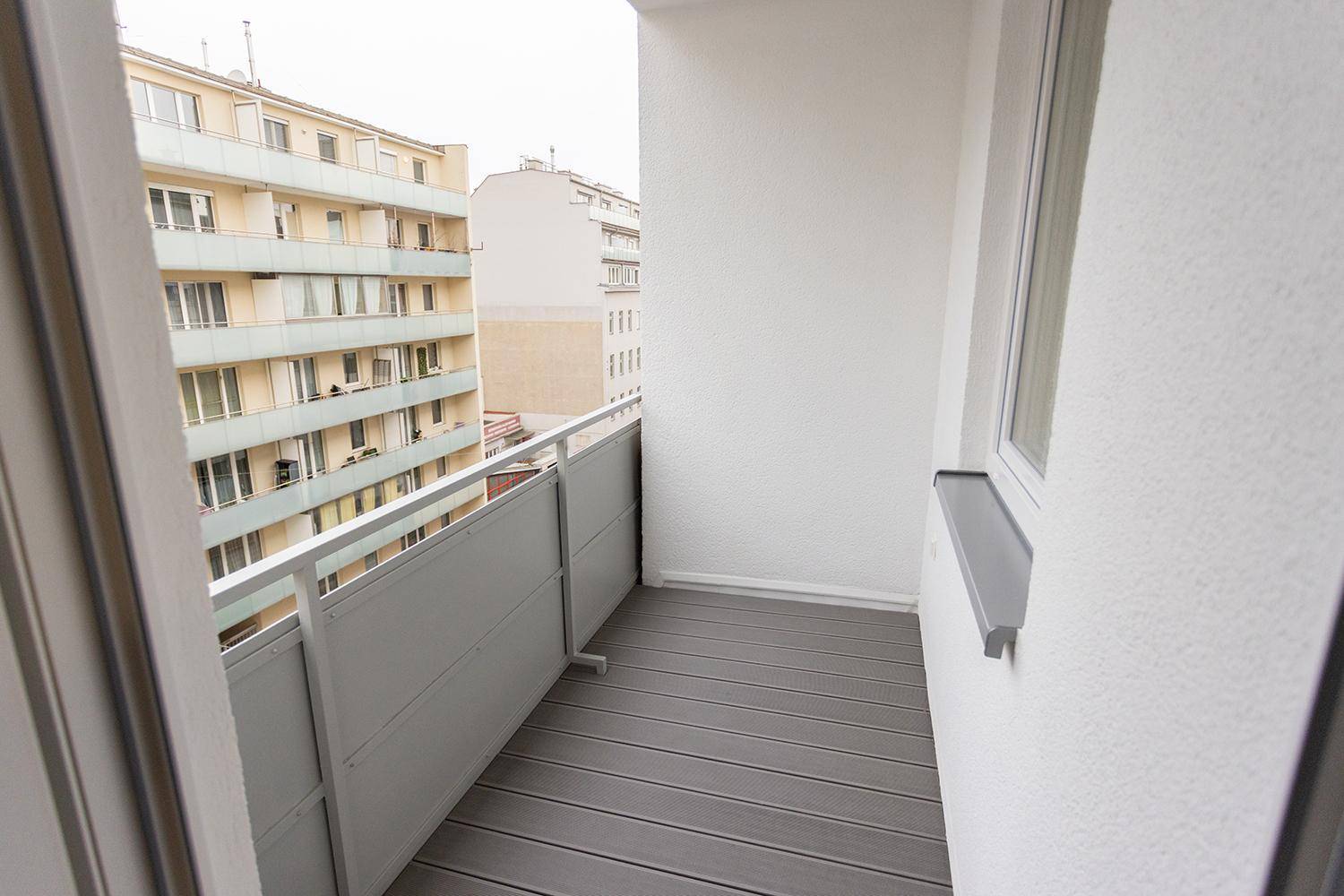 Schmaler Balkon mit grauem Bodenbelag und Blick auf die städtische Umgebung und Gebäude.