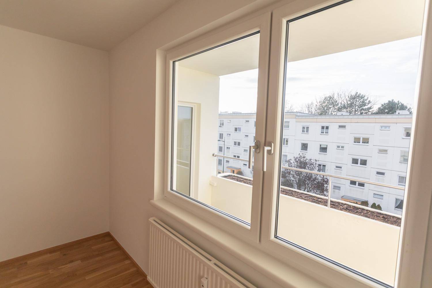 Helles Zimmer mit Parkettboden und Fenster mit Blick auf den Balkon.