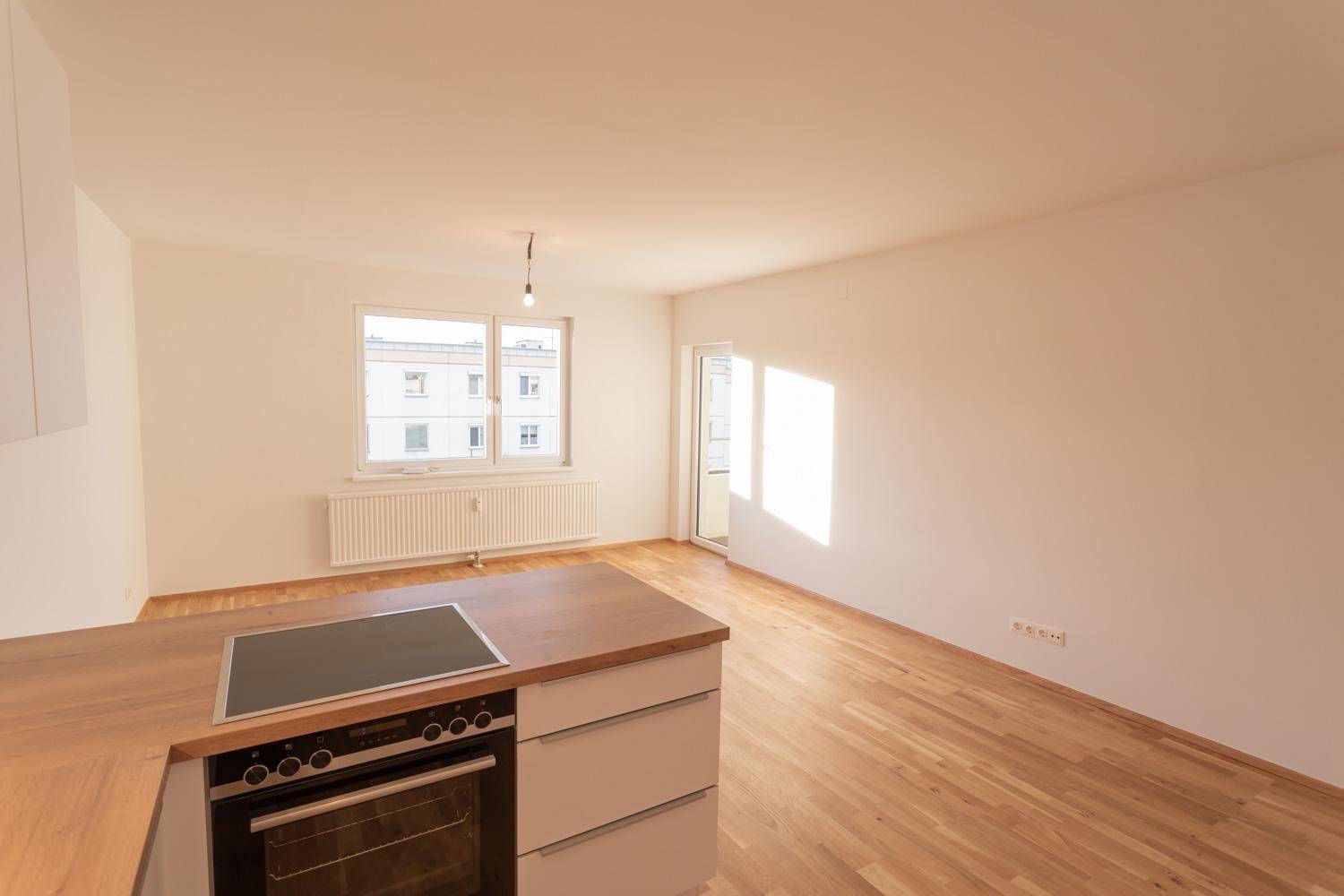 Heller offener Wohnbereich mit Kücheninsel und Zugang zum Balkon.