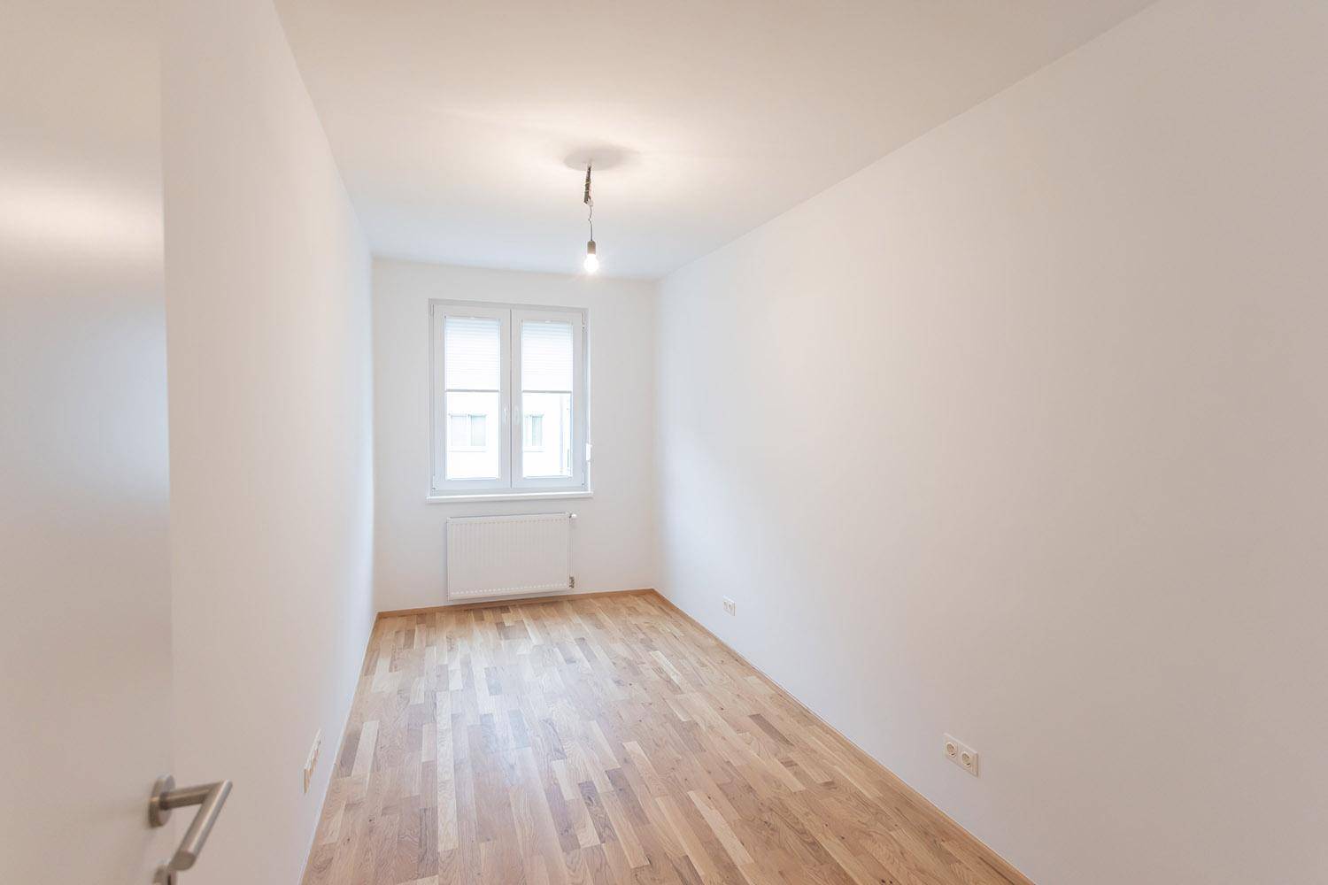 Heller, leerer Raum mit Holzboden und Fenster, vielseitig nutzbar.