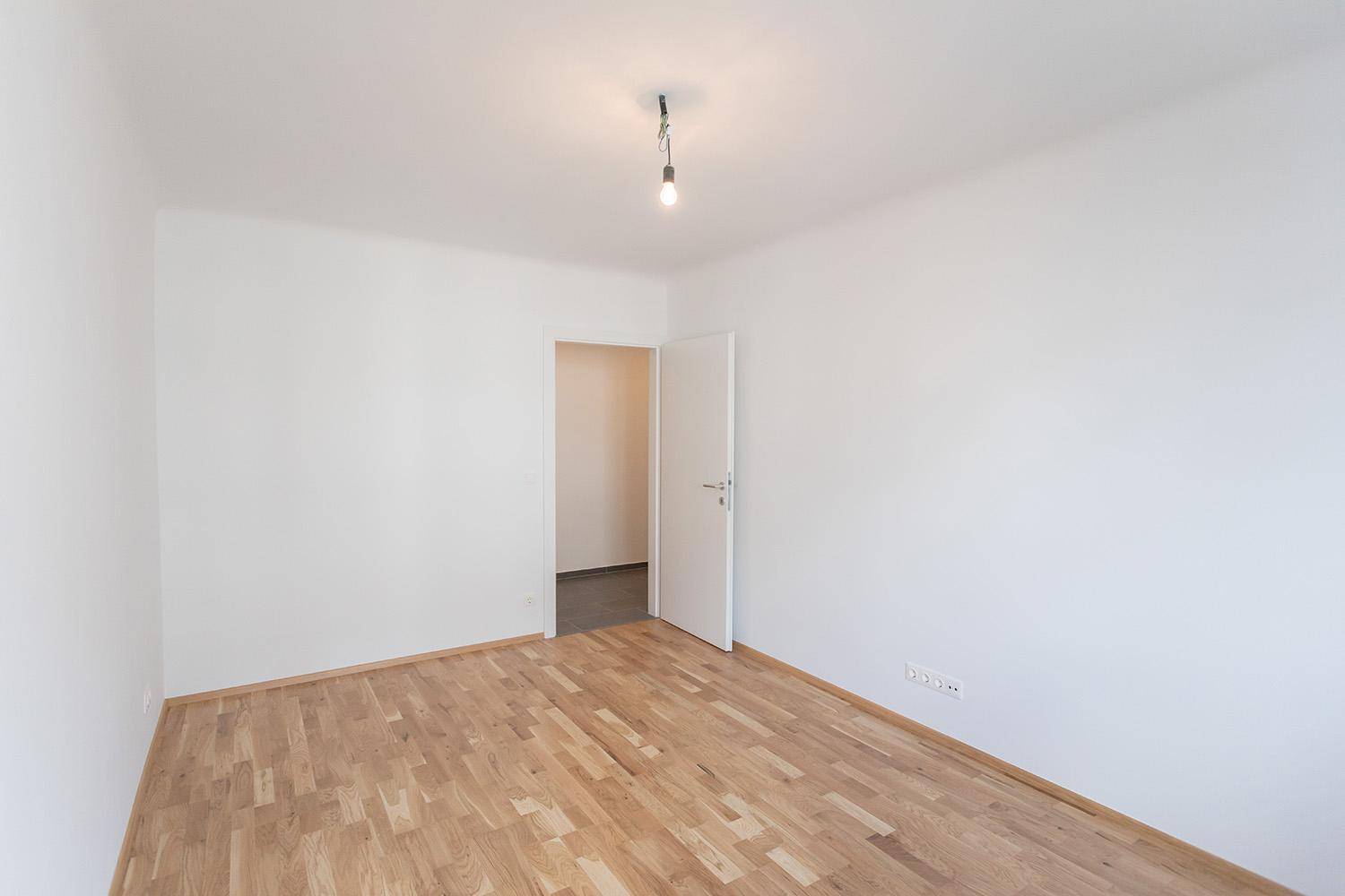 Leeres Schlafzimmer mit Parkettboden und Zugang zum Flur, bereit zur Einrichtung.