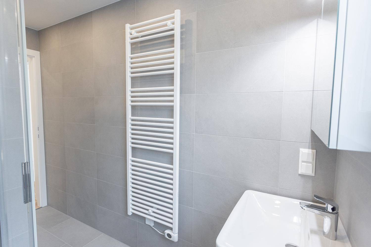 Helles Badezimmer mit modernen grauen Fliesen, einem Waschbecken und einem beheizten Handtuchhalter.