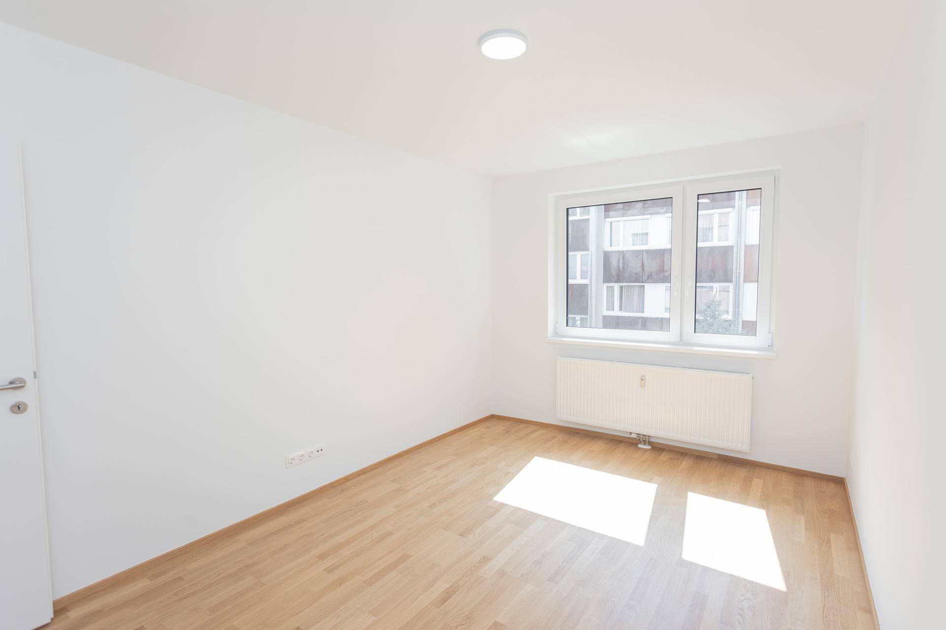 Freundliches Zimmer mit Parkettboden und großem Fenster, ideal für Schlaf- oder Arbeitszimmer.