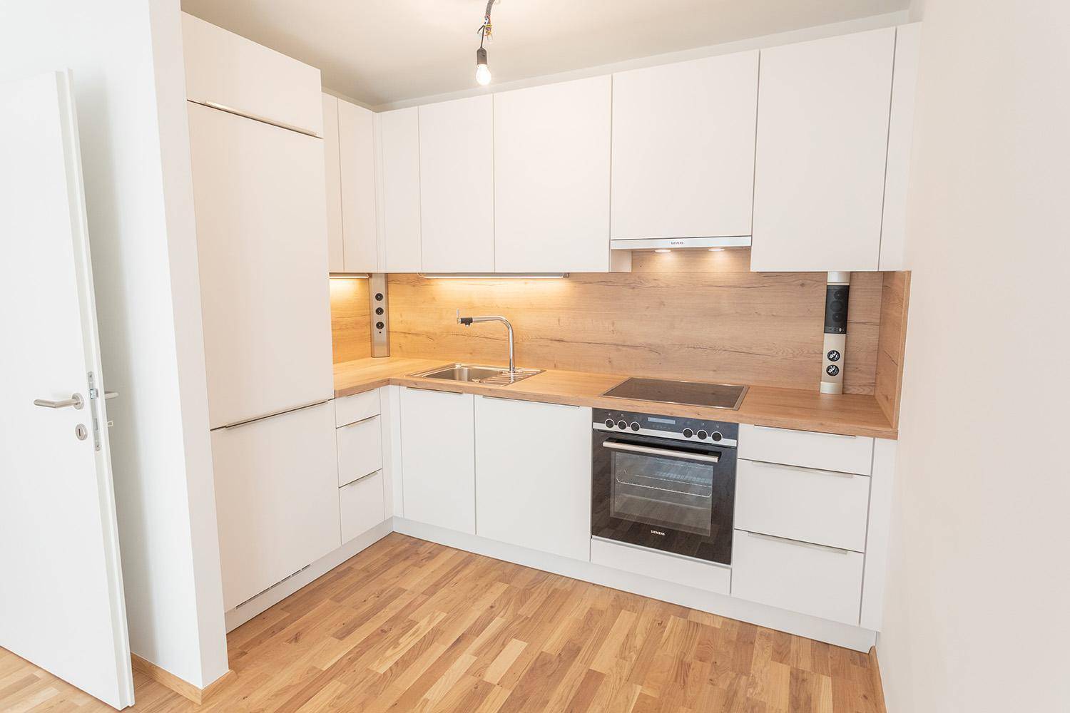 Moderne Einbauküche in Weiß mit Holzdetails und integrierten Geräten.