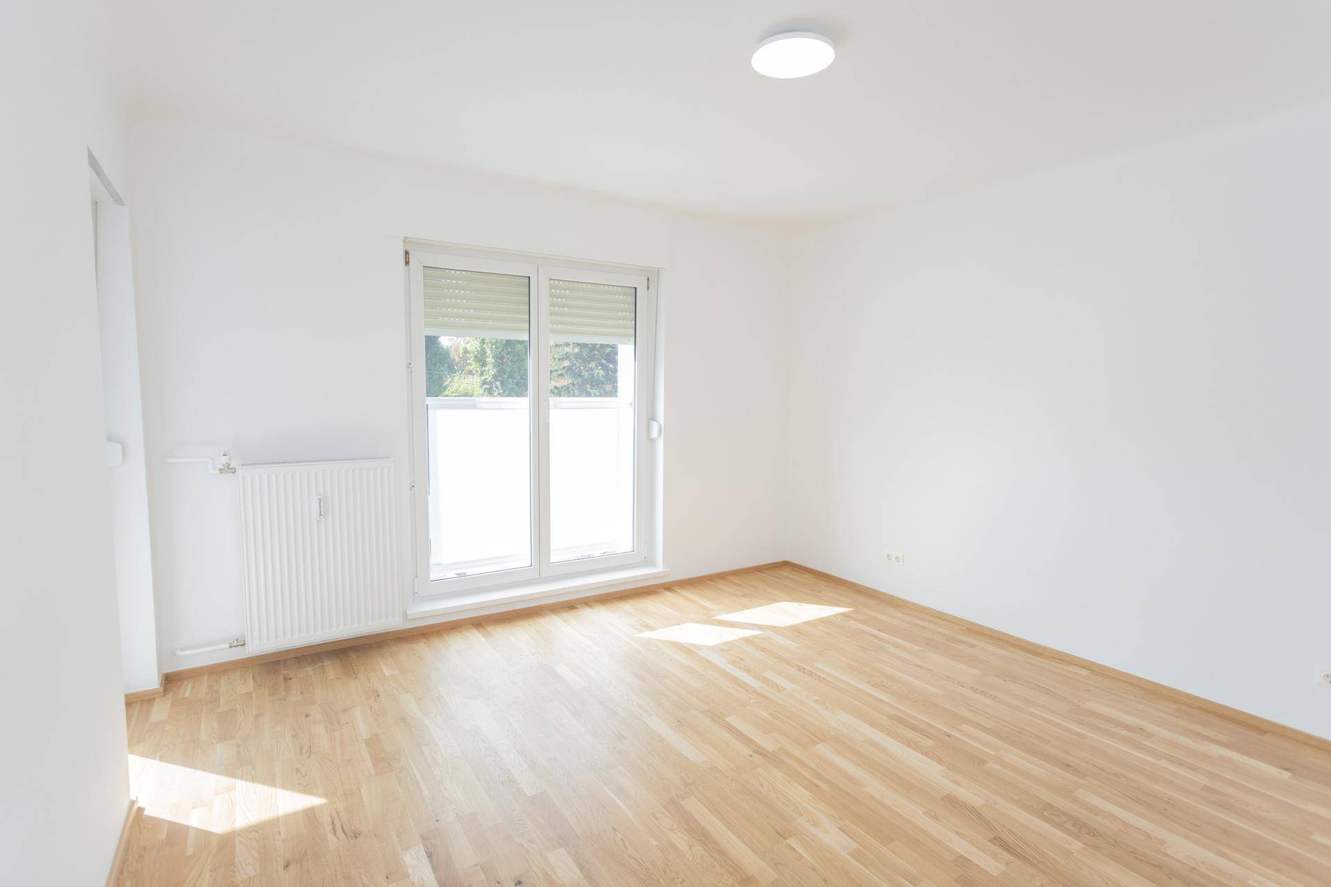 Geräumiges, helles Wohnzimmer mit Parkettboden und Zugang zu einem Balkon.