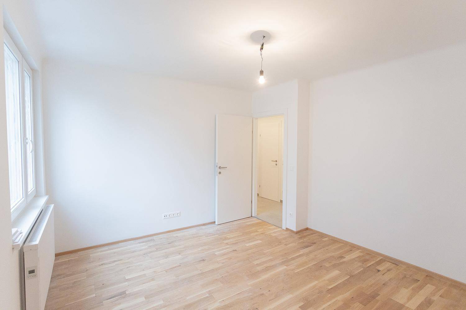 Helles Zimmer mit Parkettboden und weißer Tür, die den Zugang zum Flur ermöglicht.