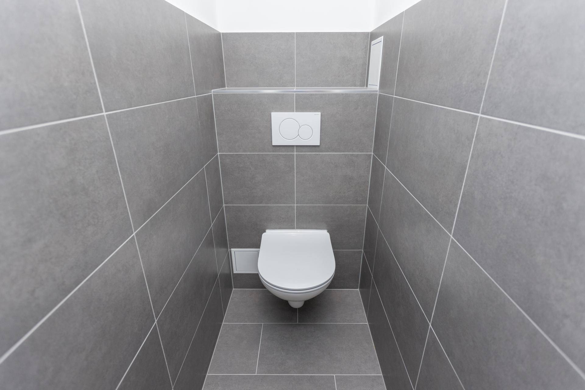 Modern gefliestes Gäste-WC mit wandhängender Toilette in neutralem Grau.