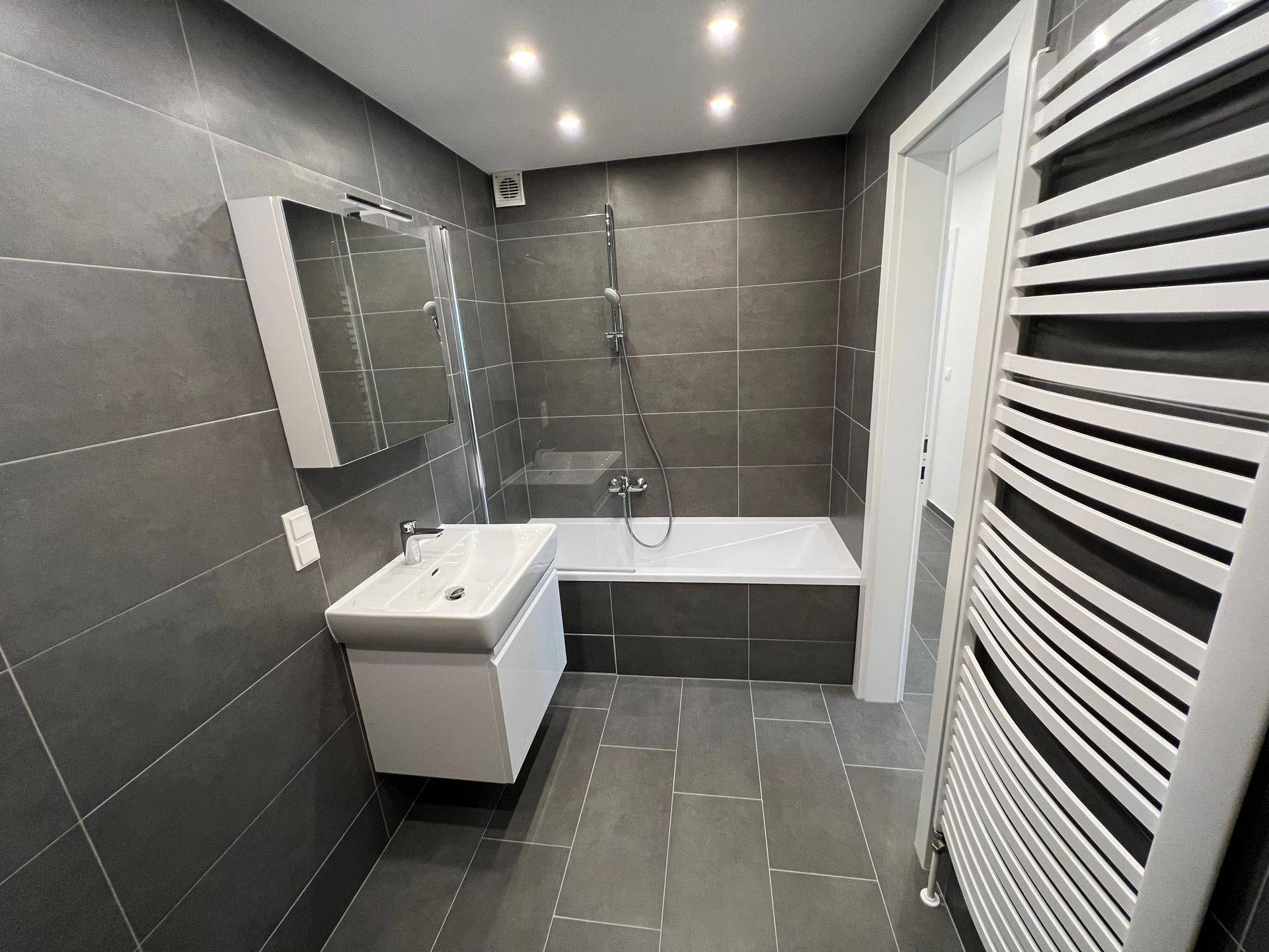 Modernes Badezimmer mit grauen Fliesen, Badewanne mit Dusche und Waschbecken, sehr gepflegt.