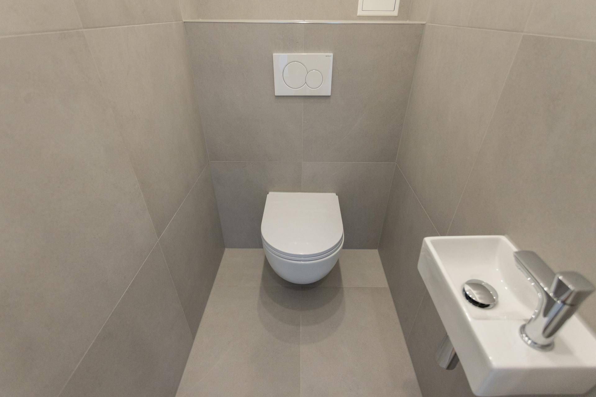 Modernes Gäste-WC mit wandhängender Toilette und kleinem Waschbecken in hellen Grautönen.