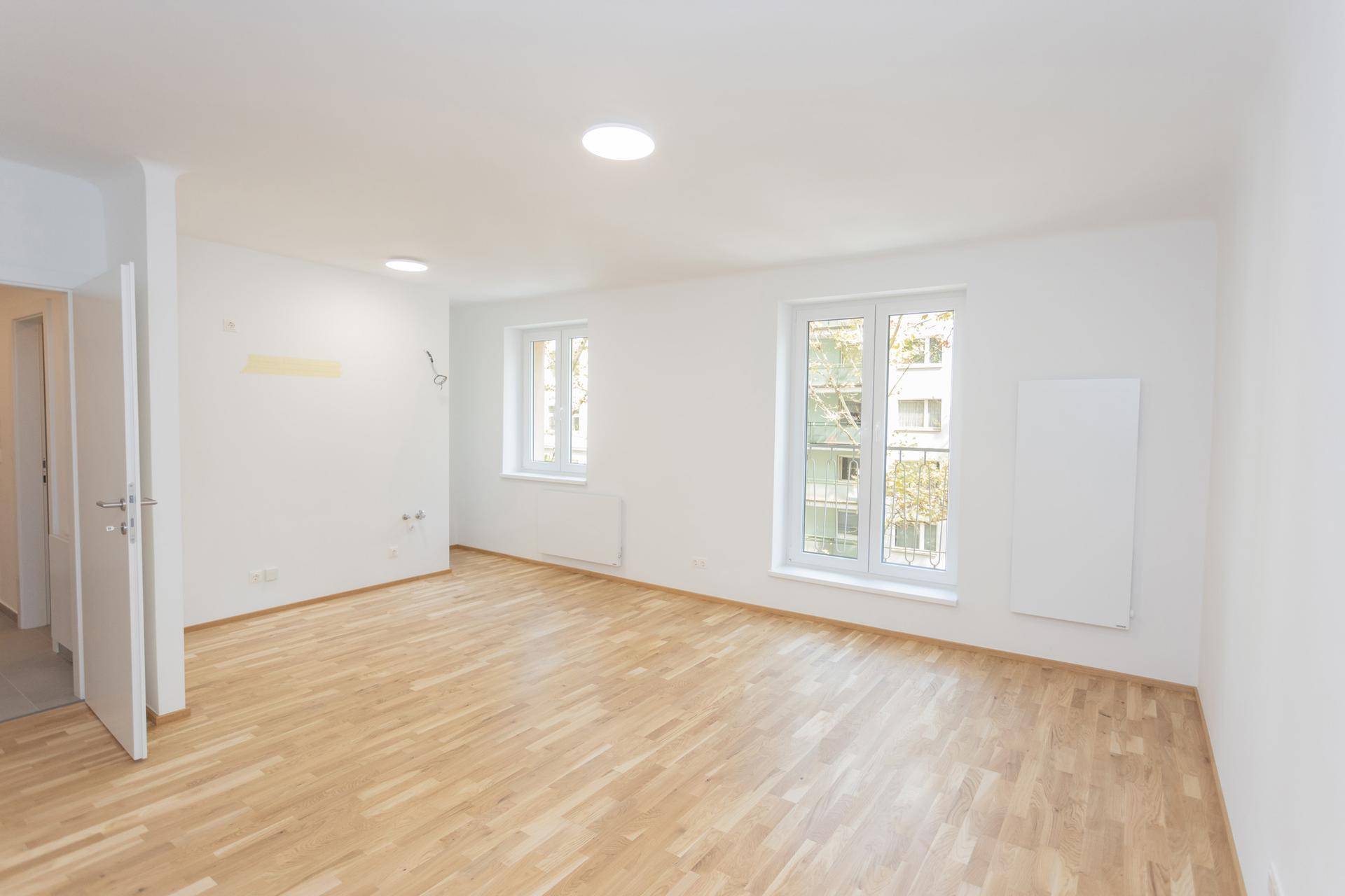 Lichtdurchflutetes Wohnzimmer mit zwei Fenstern und neu verlegtem Parkettboden.