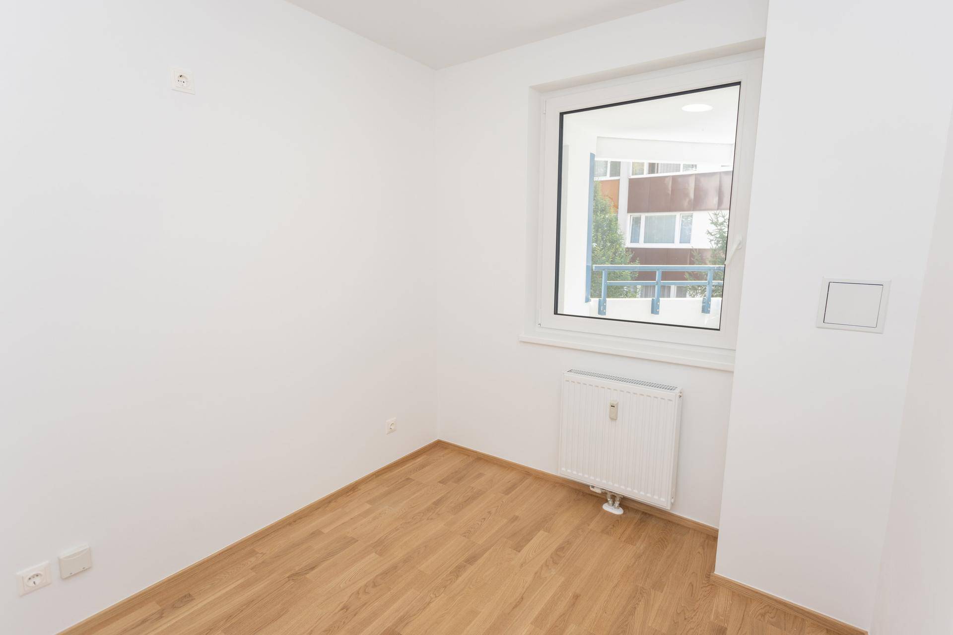 Freundliches Zimmer mit Parkettboden und großem Fenster, ideal für Schlaf- oder Arbeitszimmer.