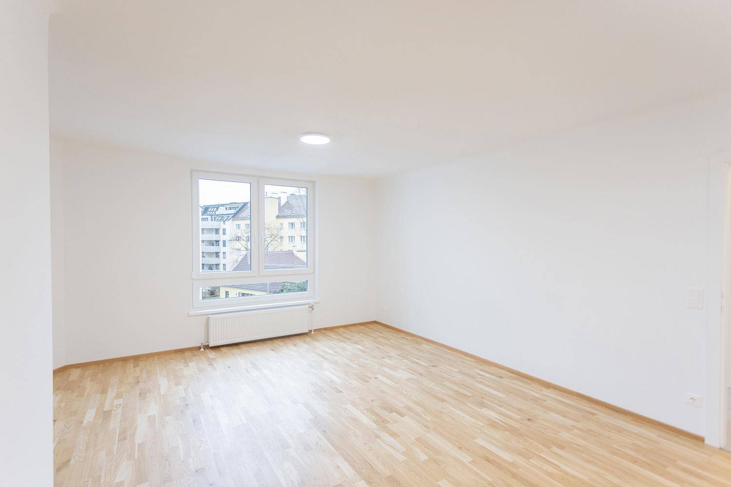 Helles Wohnzimmer mit Holzboden und großem Fenster, das viel Tageslicht hereinlässt.