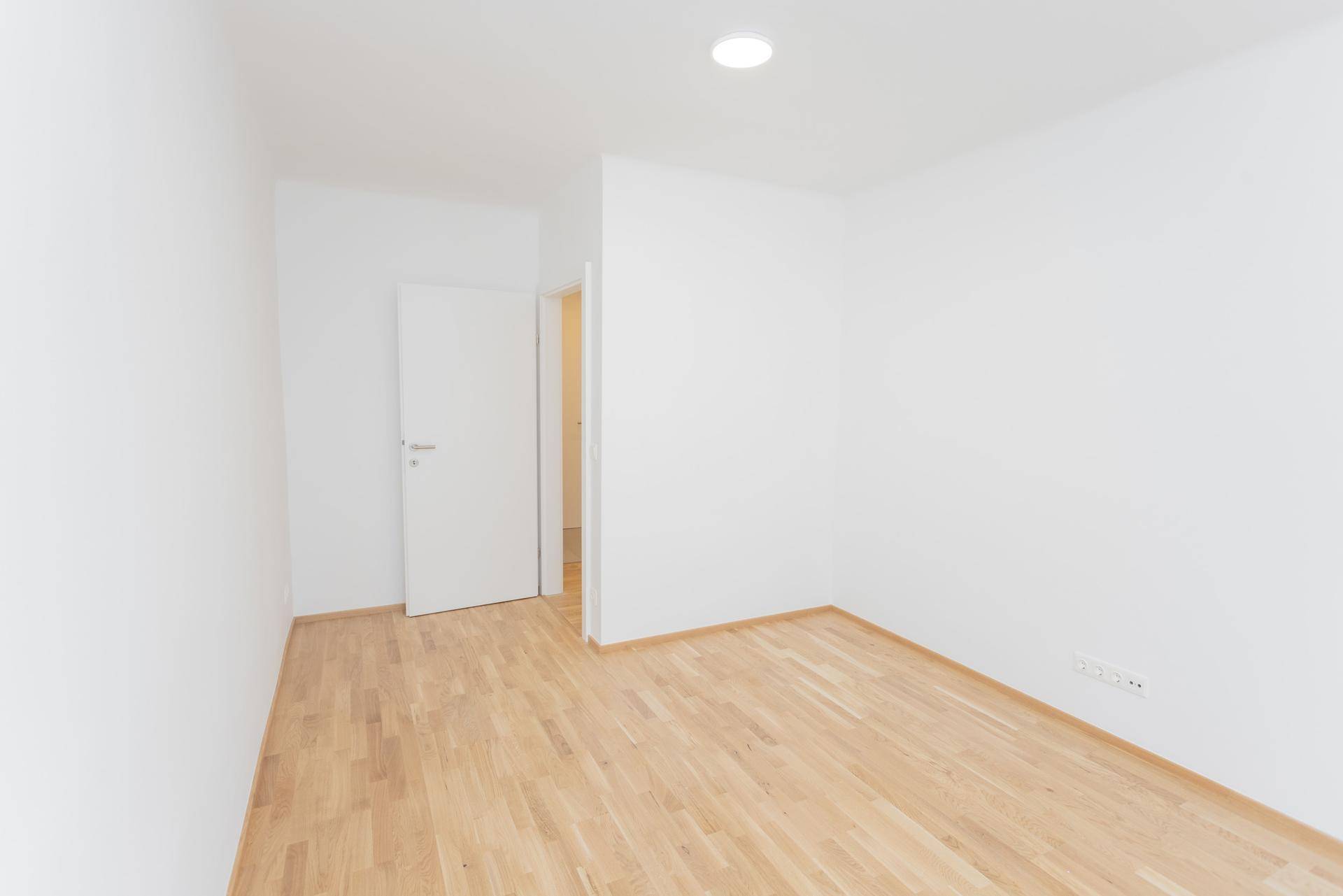 Heller, leerer Raum mit Holzfußboden und weiß gestrichenen Wänden.