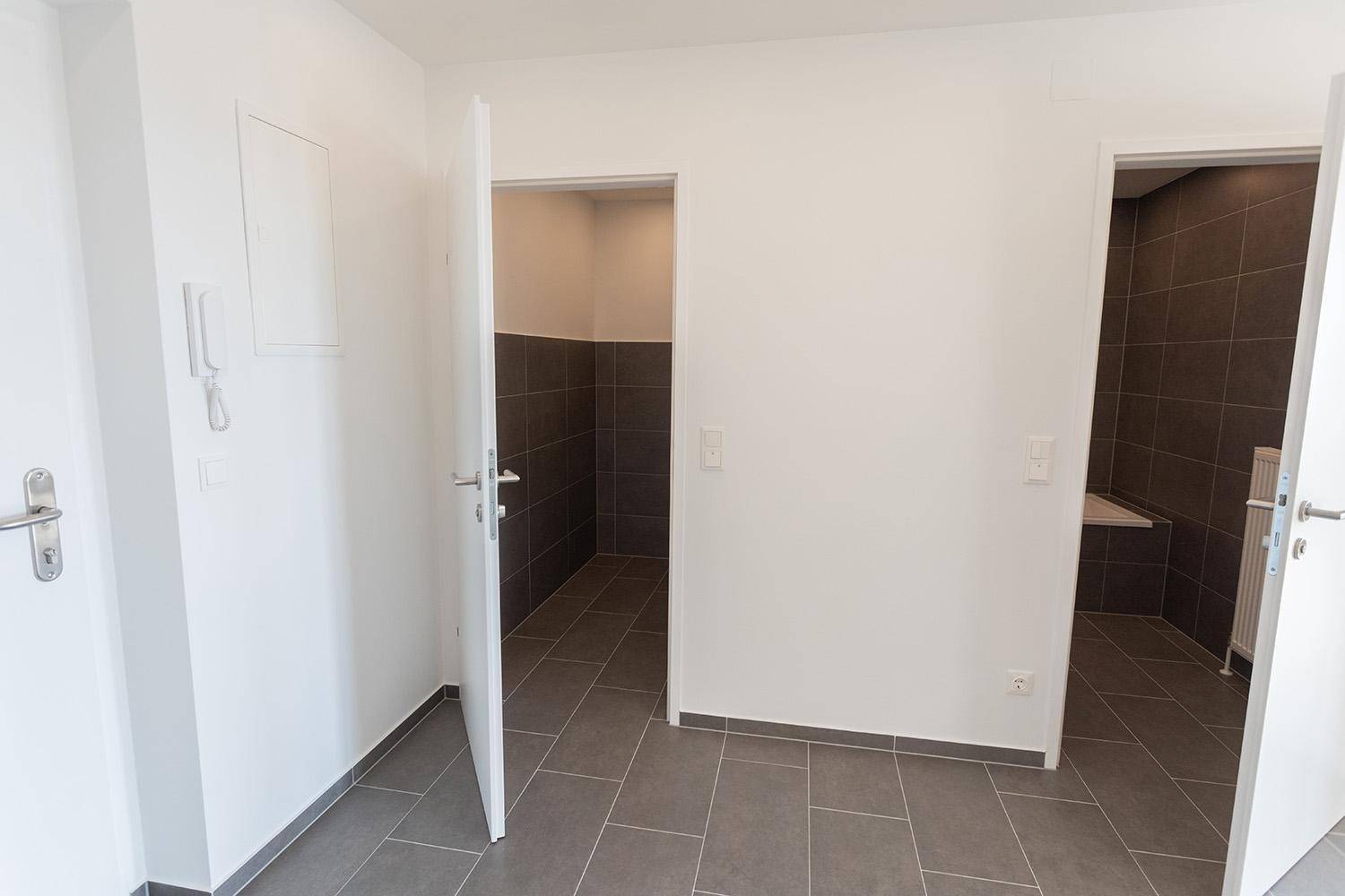 Flur mit offenen Türen, die den Zugang zu gefliesten Sanitärbereichen ermöglichen.