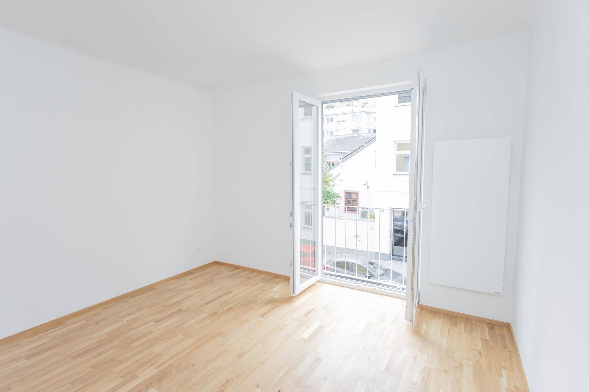 Heller, leerer Raum mit Holzfußboden und Zugang zu einem französischen Balkon.