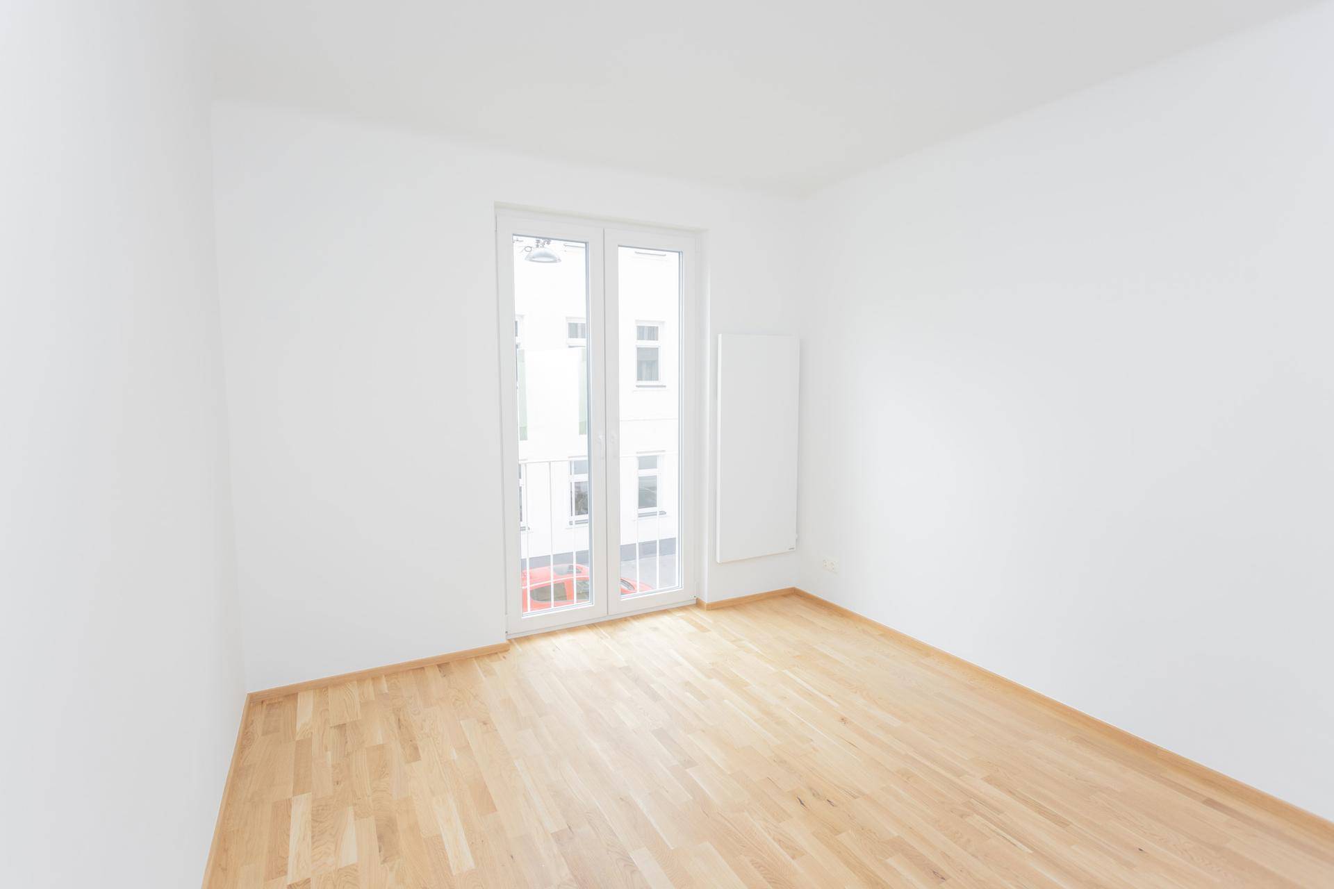 Heller, leerer Raum mit Holzfußboden und Zugang zu einem französischen Balkon.