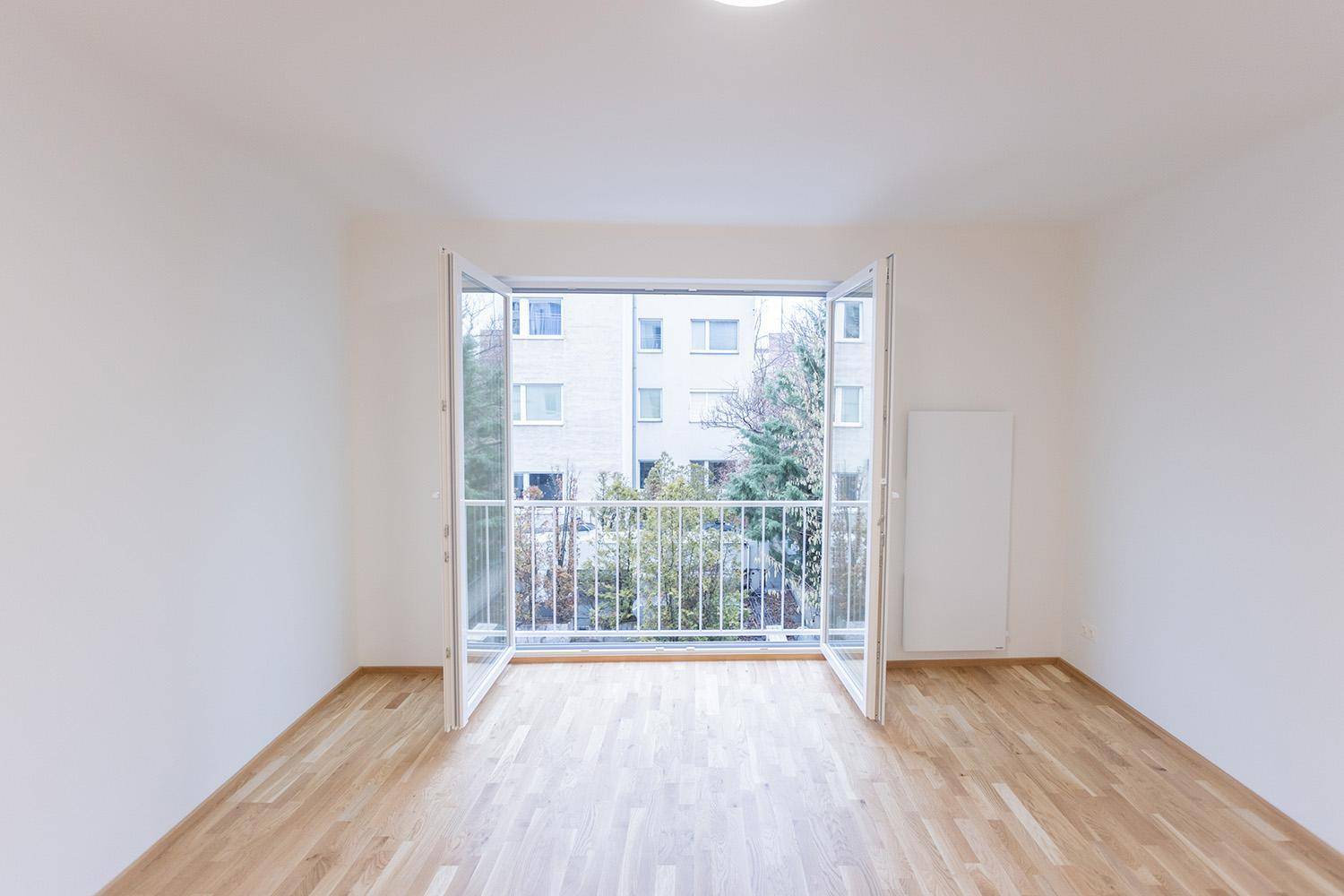 Helles Zimmer mit Parkettboden und Zugang zu einem kleinen Balkon mit Blick ins Grüne.
