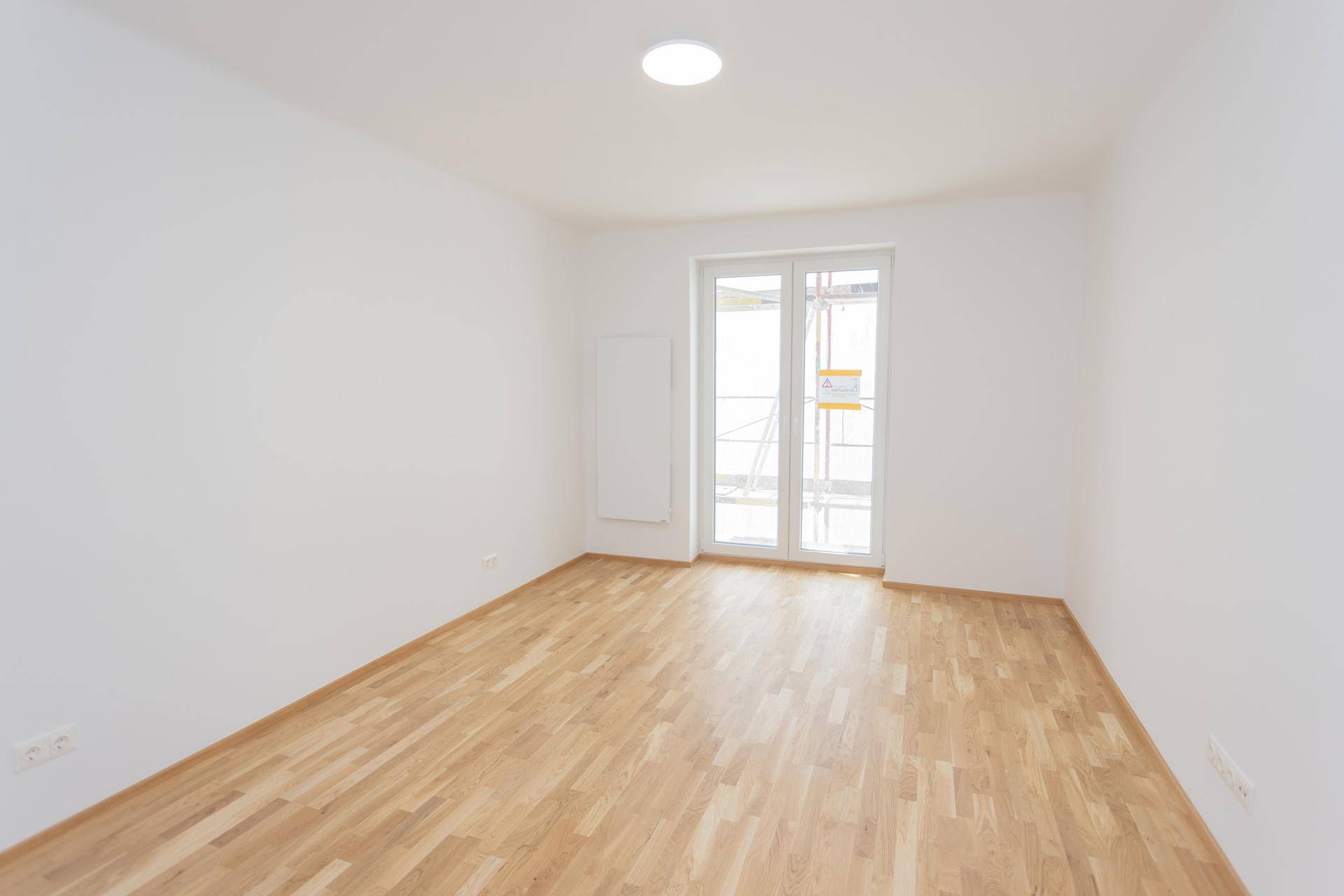 Wohnraum mit Parkettboden und Zugang zu einem Balkon, der noch im Bau ist.