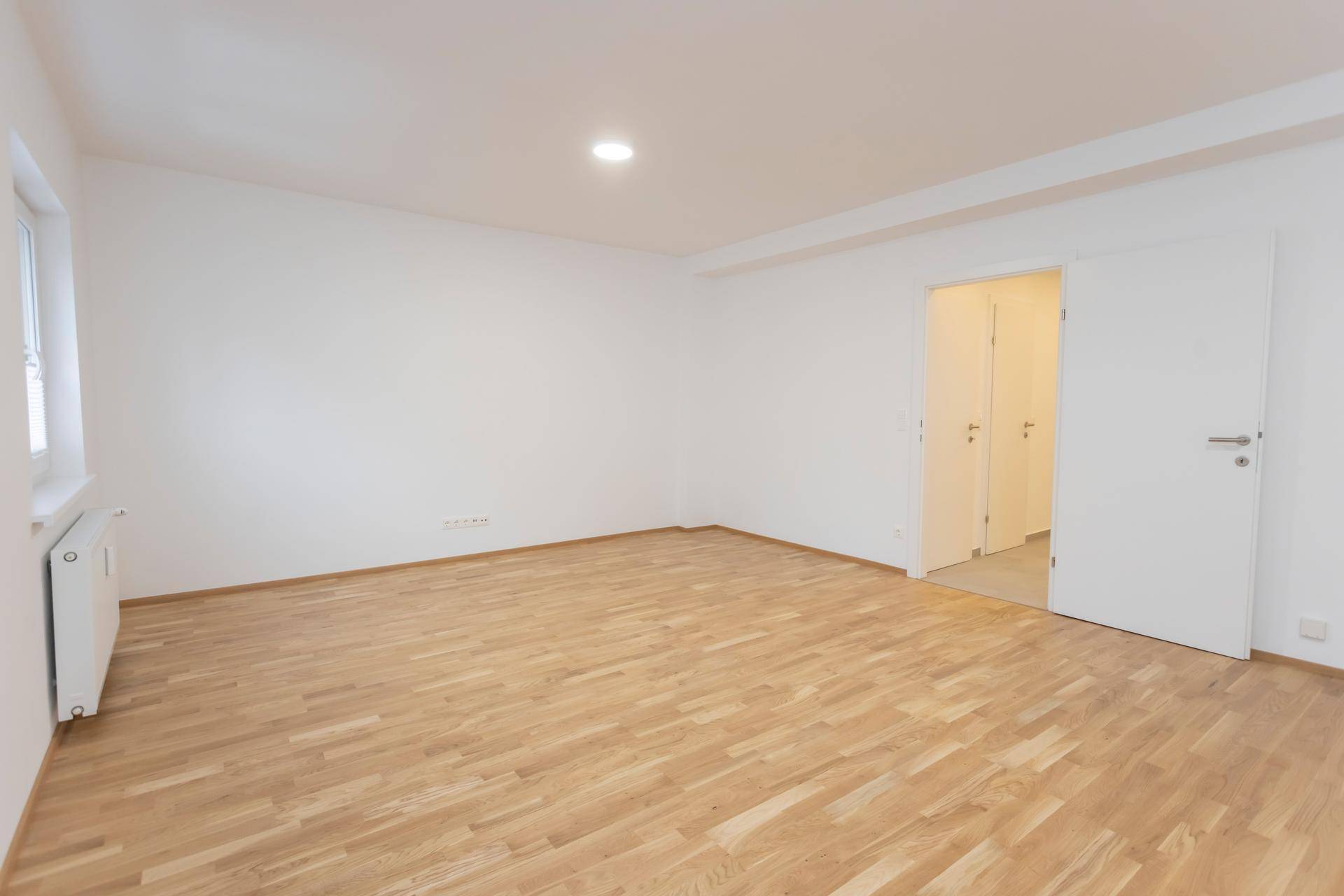 Geräumiger, heller Raum mit Parkettboden und Zugang zu einem weiteren Zimmer.