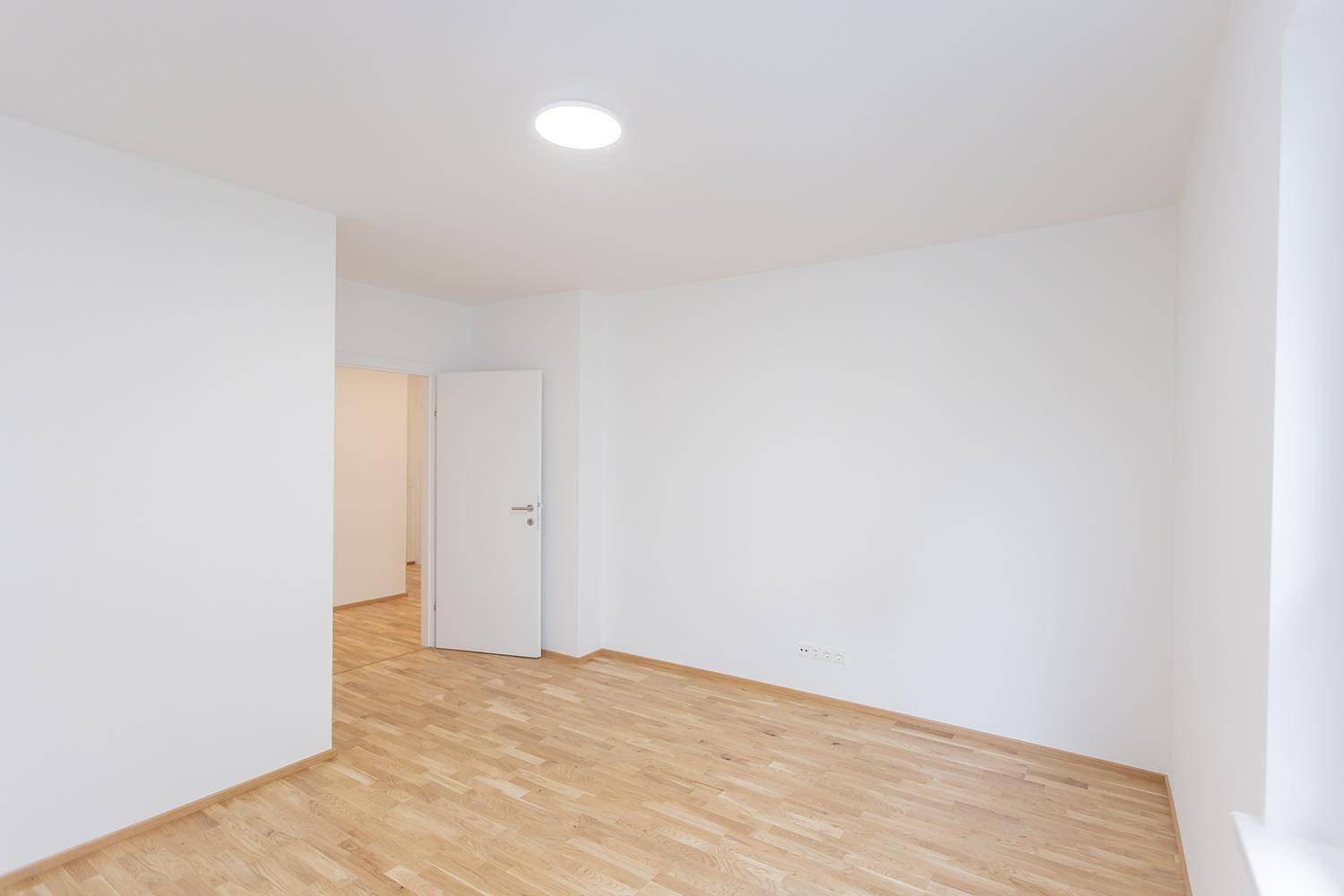 Leerer Raum mit Holzparkettboden und weiß gestrichenen Wänden, ideal für ein Schlafzimmer.