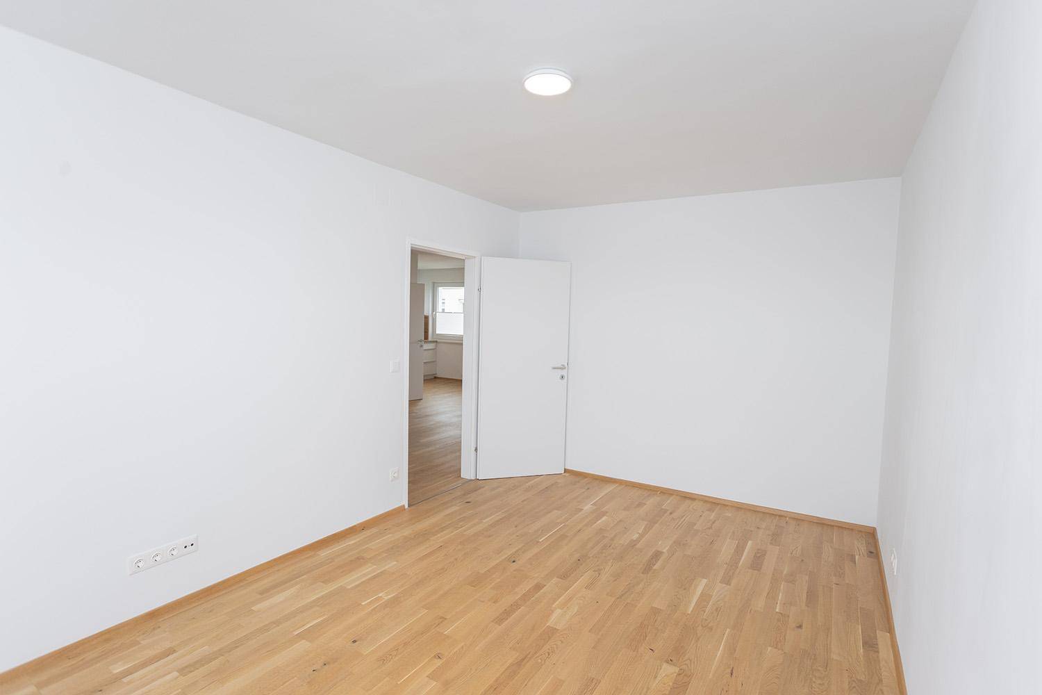 Leeres Zimmer mit Eichenparkett und weiß gestrichenen Wänden, vielseitig nutzbar.