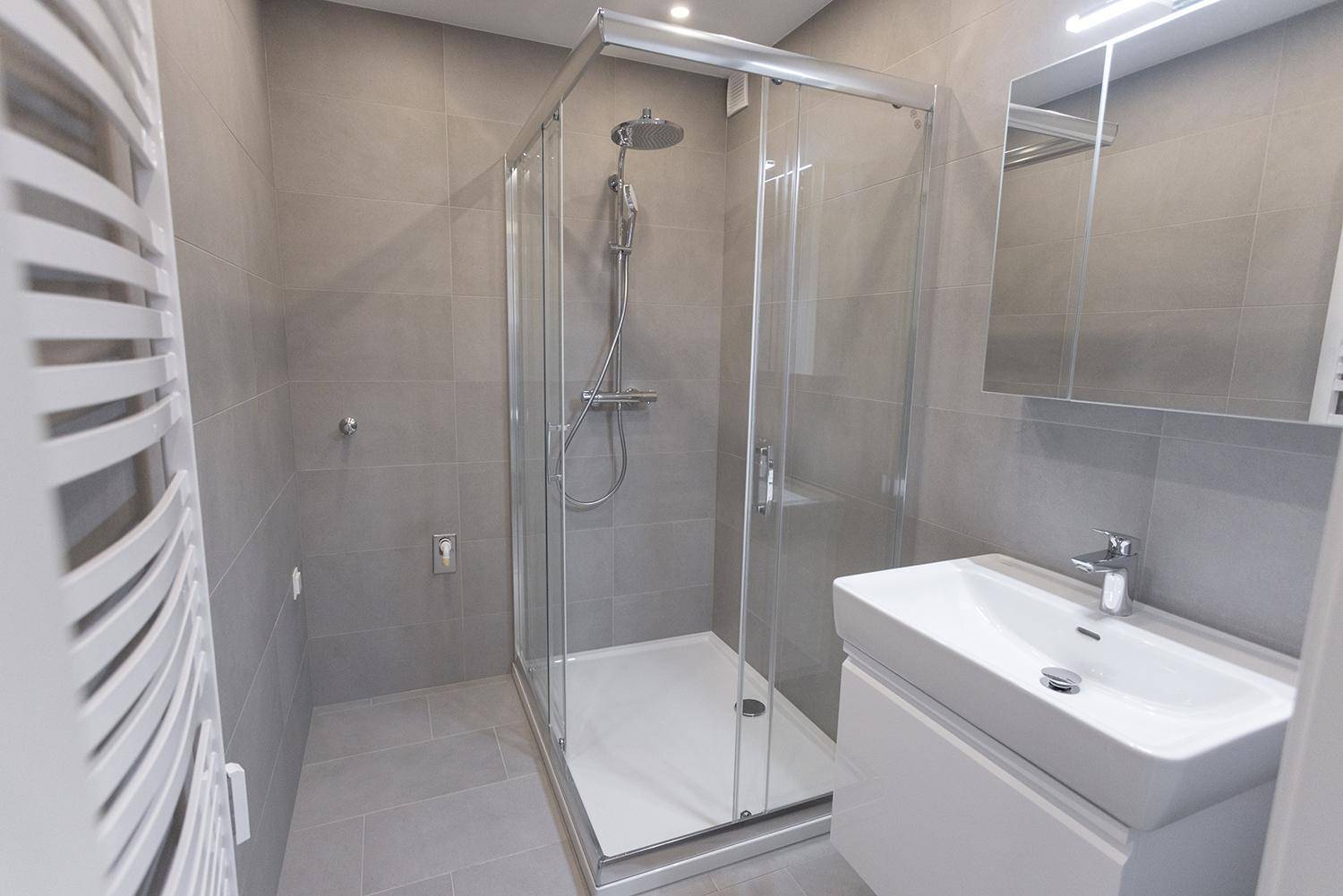 Modernes Badezimmer mit Duschkabine, Waschbecken und beheiztem Handtuchhalter.