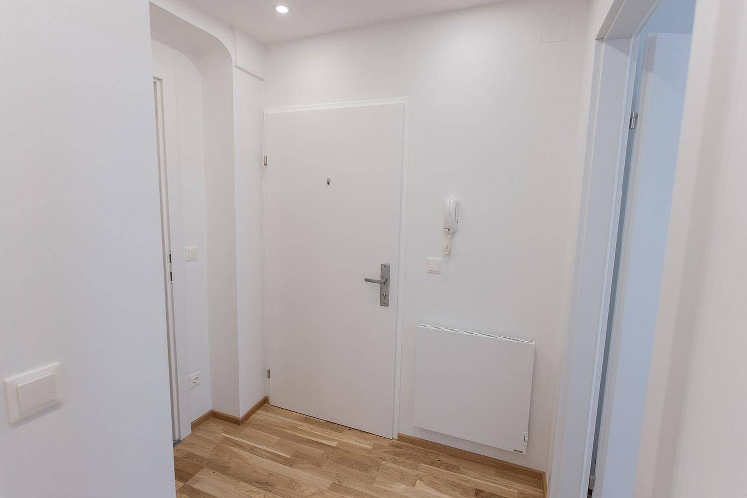 Heller Eingangsbereich mit Holzboden, weißer Tür und Gegensprechanlage.