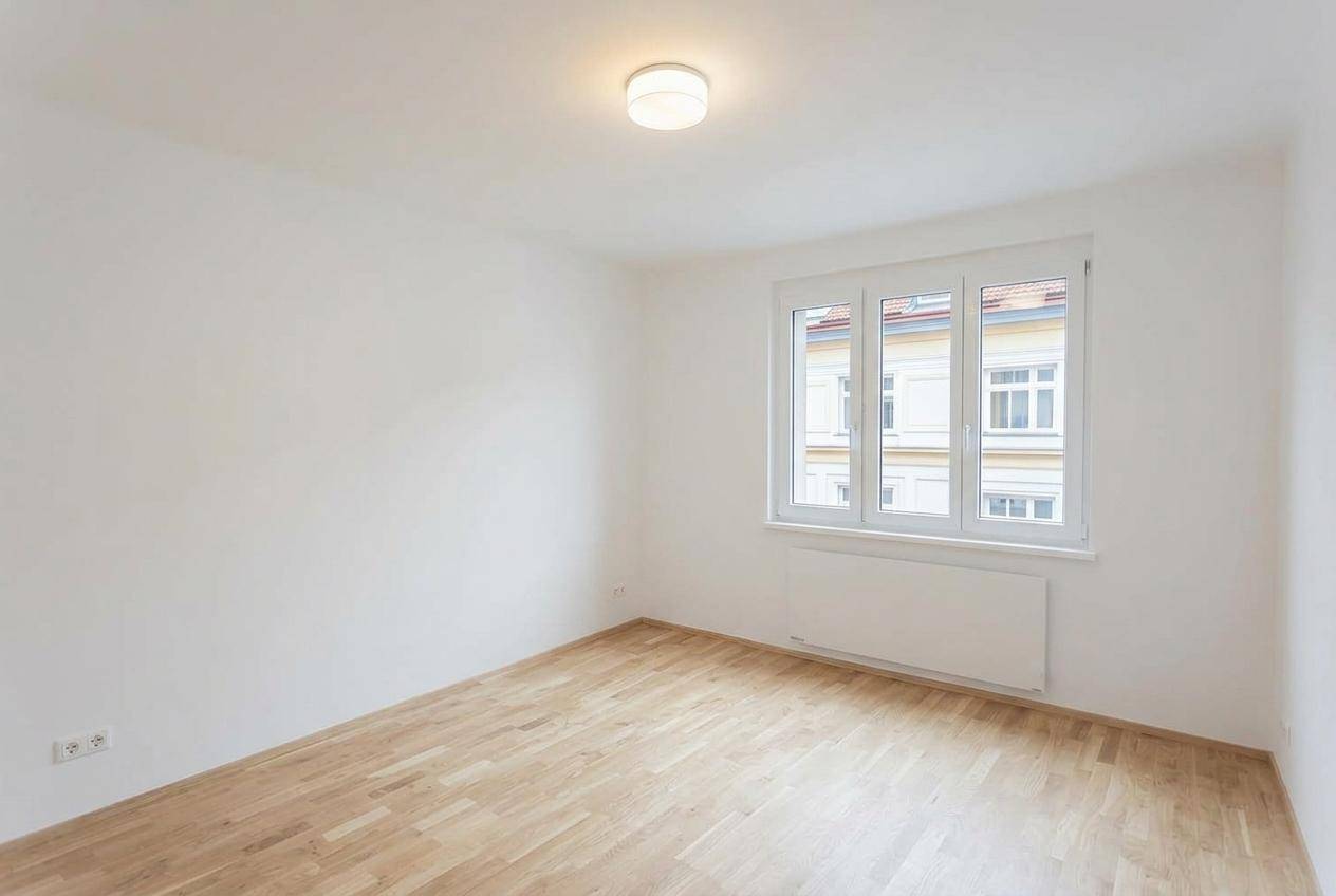 Heller, leerer Raum mit Parkettboden, weißen Wänden und einem großen Fenster mit Ausblick.