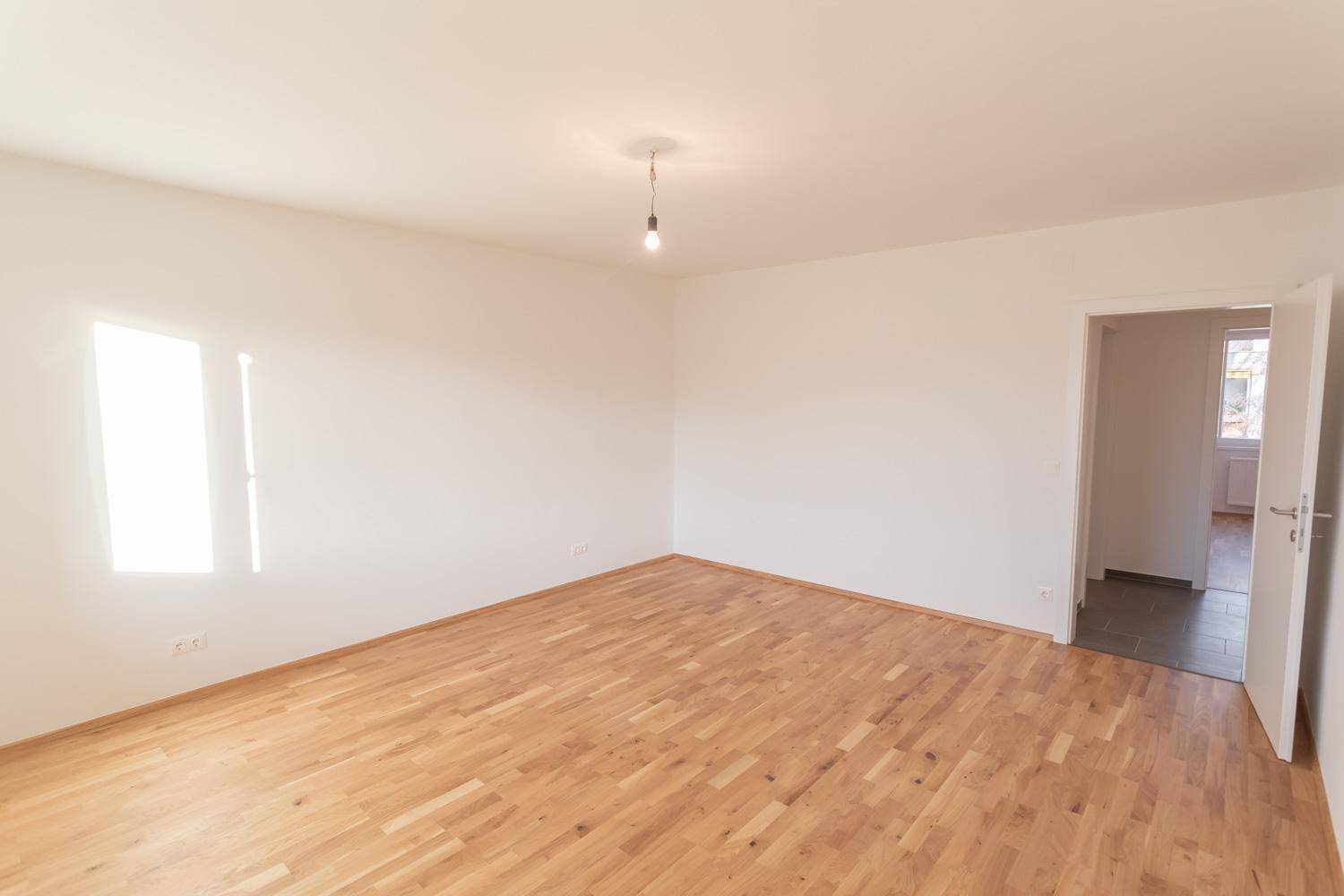 Geräumiges, leeres Zimmer mit Parkettboden und Zugang zu einem weiteren Raum.