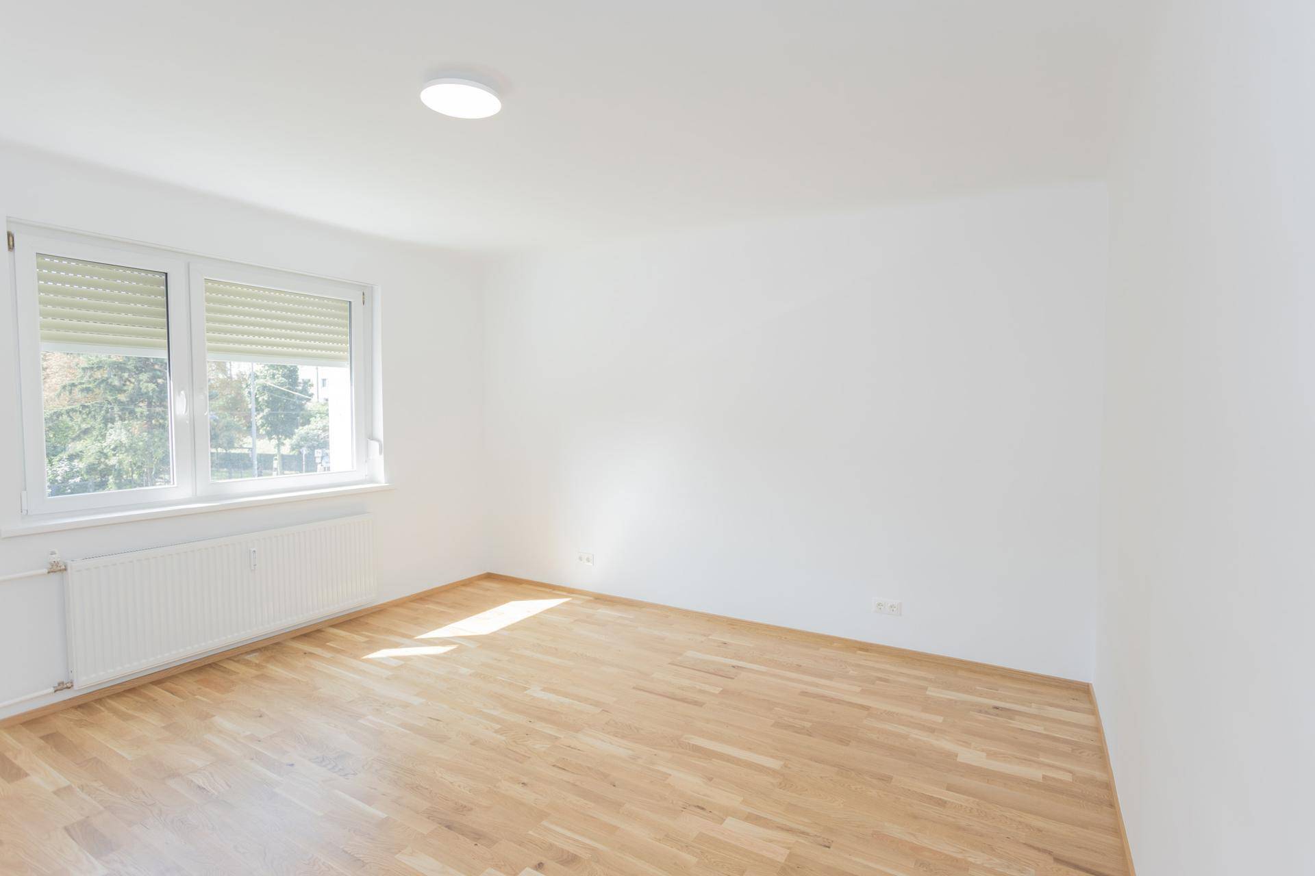 Leeres, helles Schlafzimmer mit Holzboden und Fenster, das einen Blick nach draußen bietet.