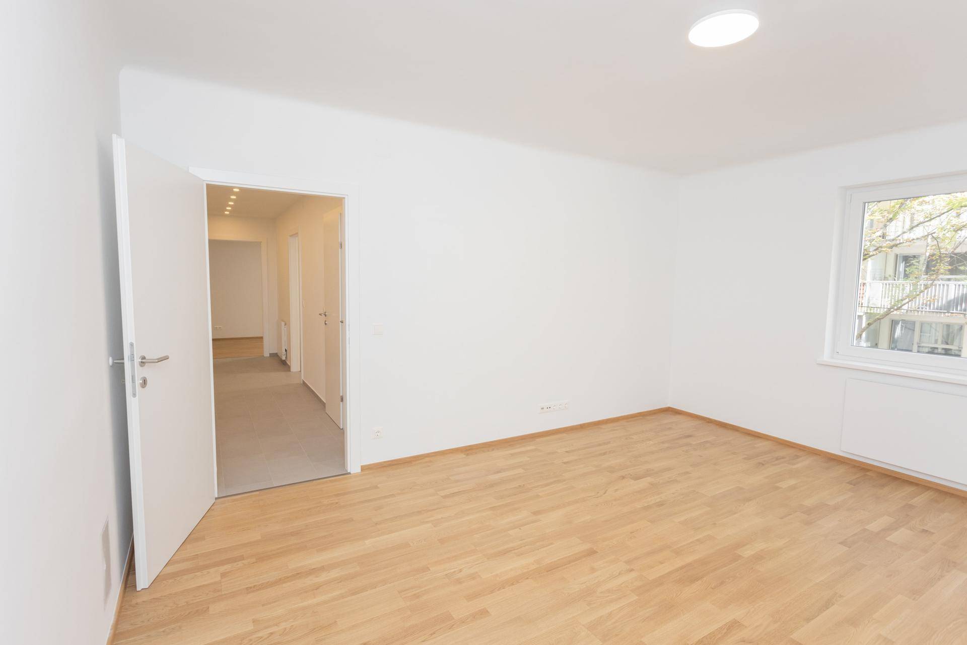 Leeres Wohnzimmer mit Holzparkettboden und offener Tür zum Flur, bereit zur Einrichtung.