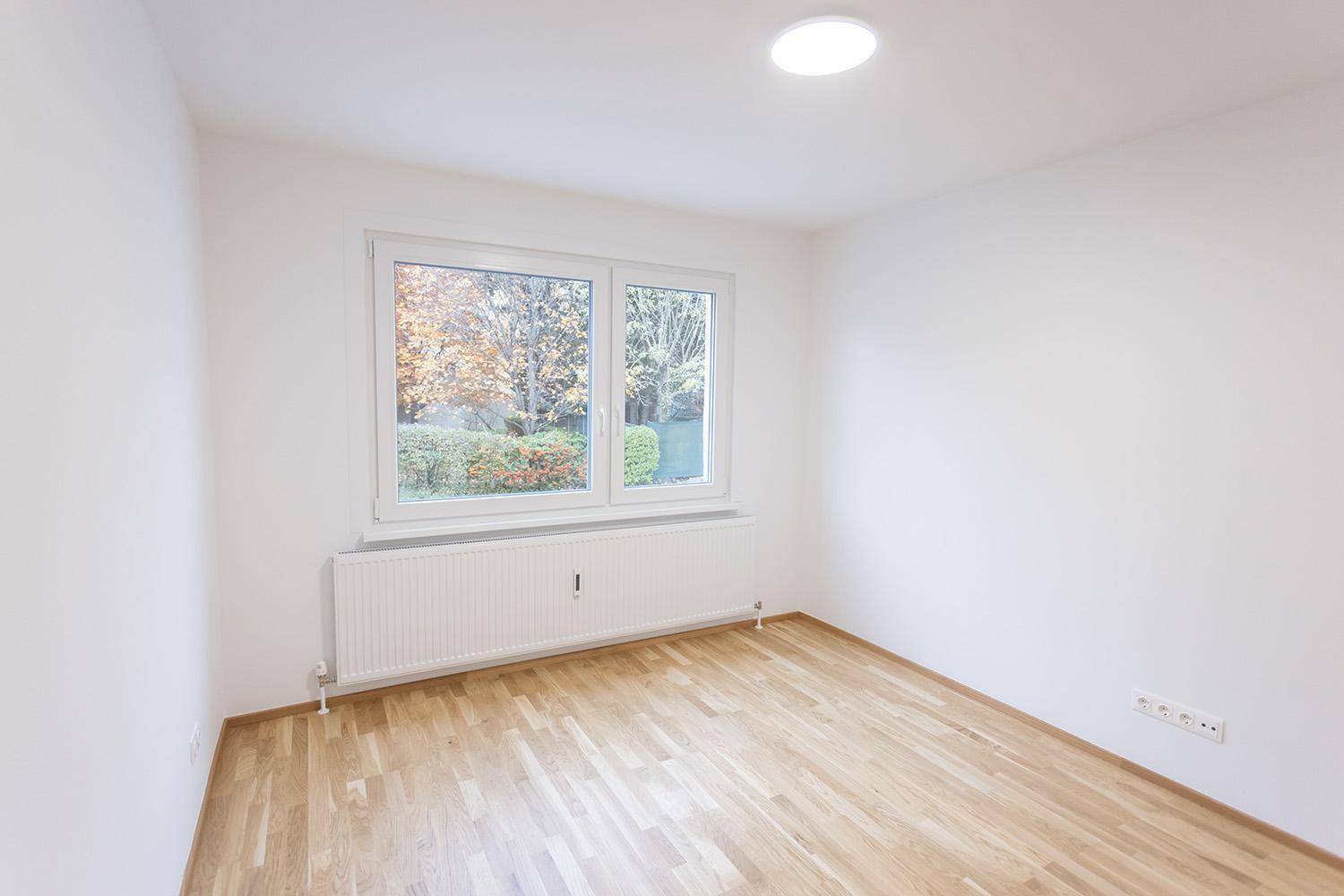 Helles, unmöbliertes Zimmer mit Parkettboden und Blick ins Grüne, ideal als Schlafzimmer.