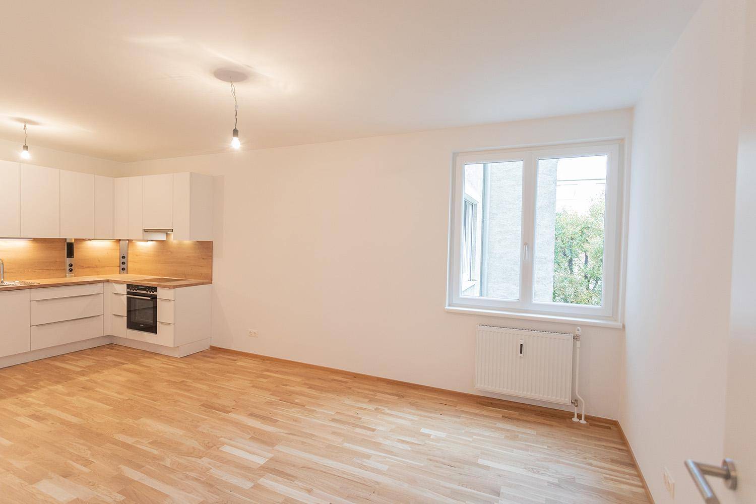 Offener Wohnbereich mit Einbauküche und Fenster, das viel Tageslicht hereinlässt.