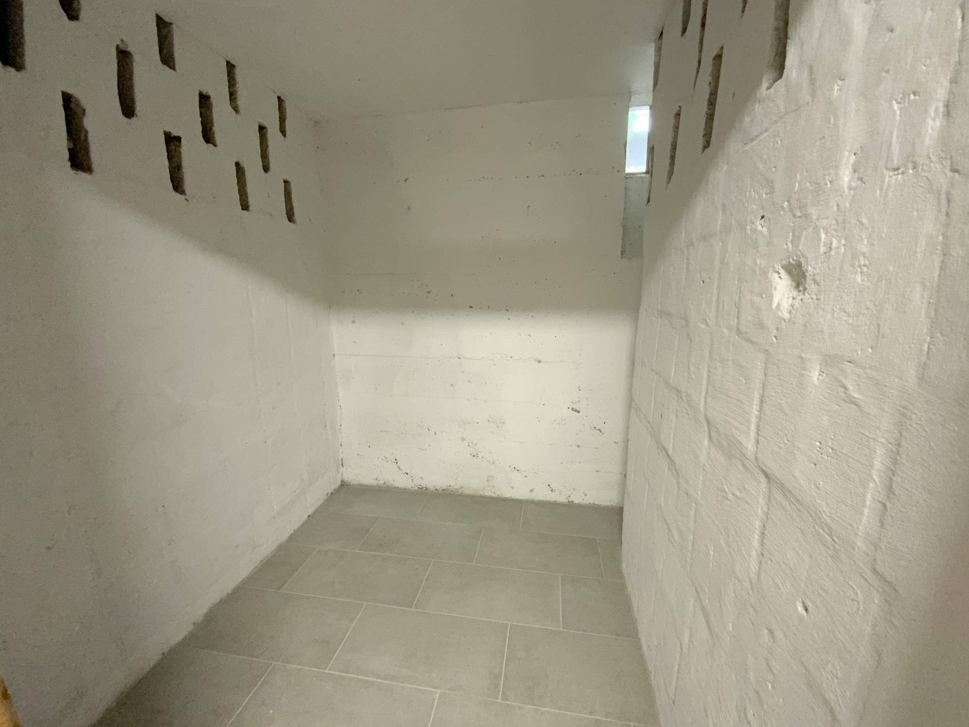 Funktionaler Abstellraum im Keller mit gefliestem Boden und Belüftungsschlitzen.