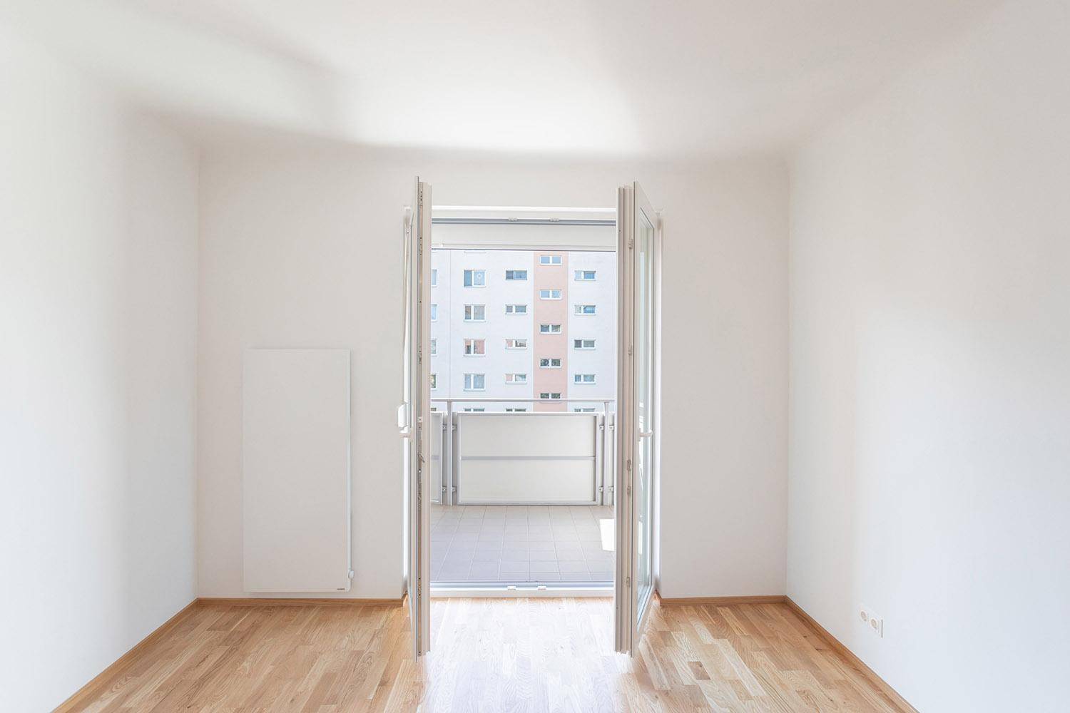 Geräumiger, heller Raum mit Parkettboden und weit geöffneten Balkontüren.