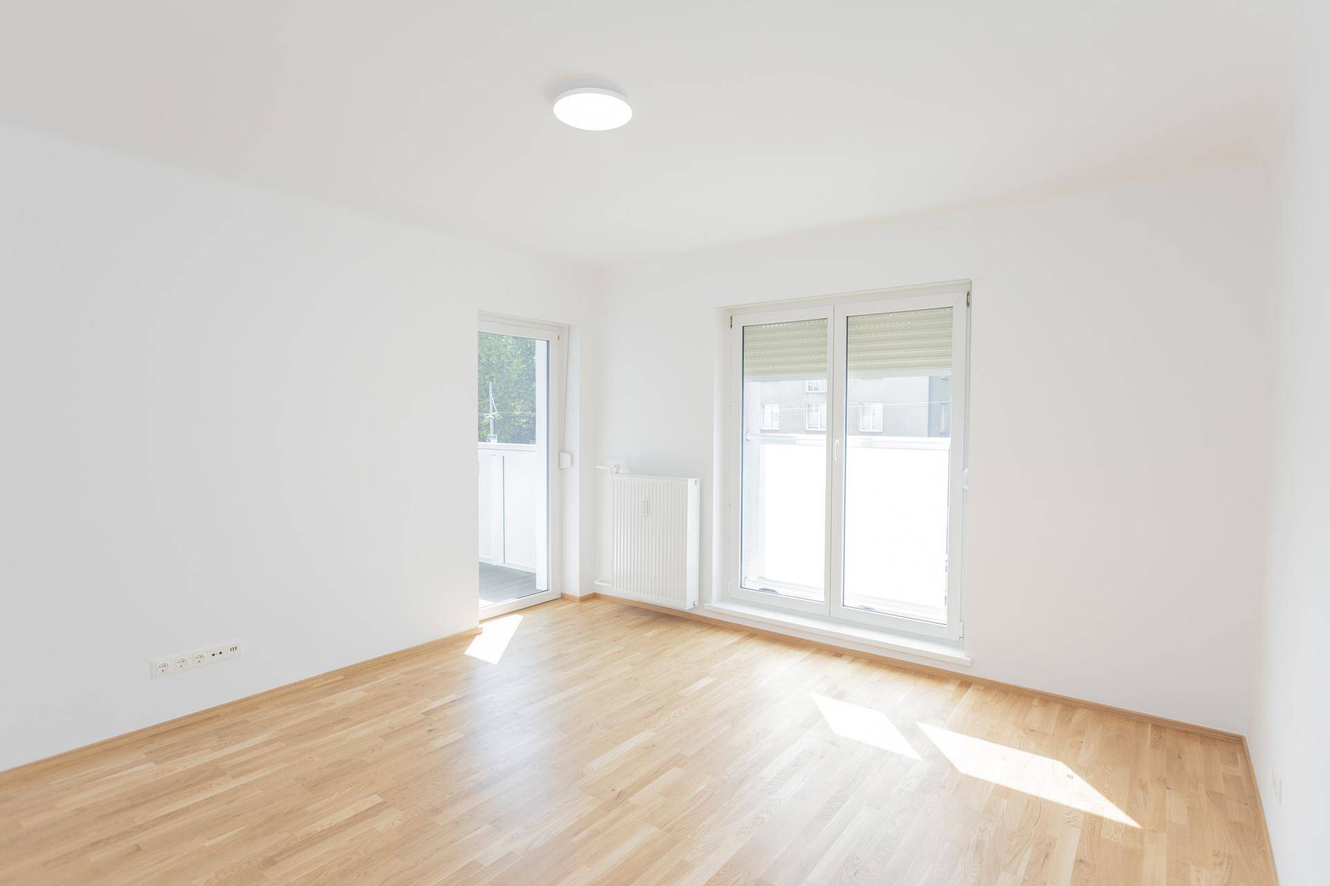 Helles Wohnzimmer mit Parkettboden, großem Fenster und Zugang zum Balkon.
