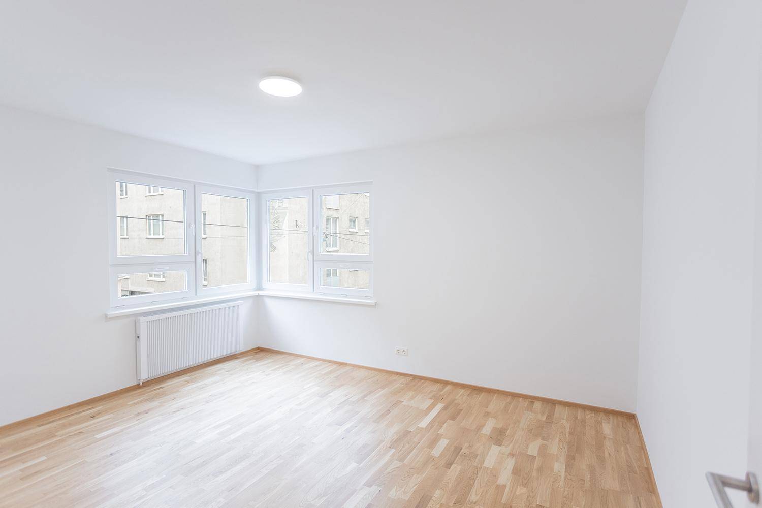 Heller Raum mit Holzparkettboden und großen Fenstern, ideal als Schlaf- oder Arbeitszimmer.