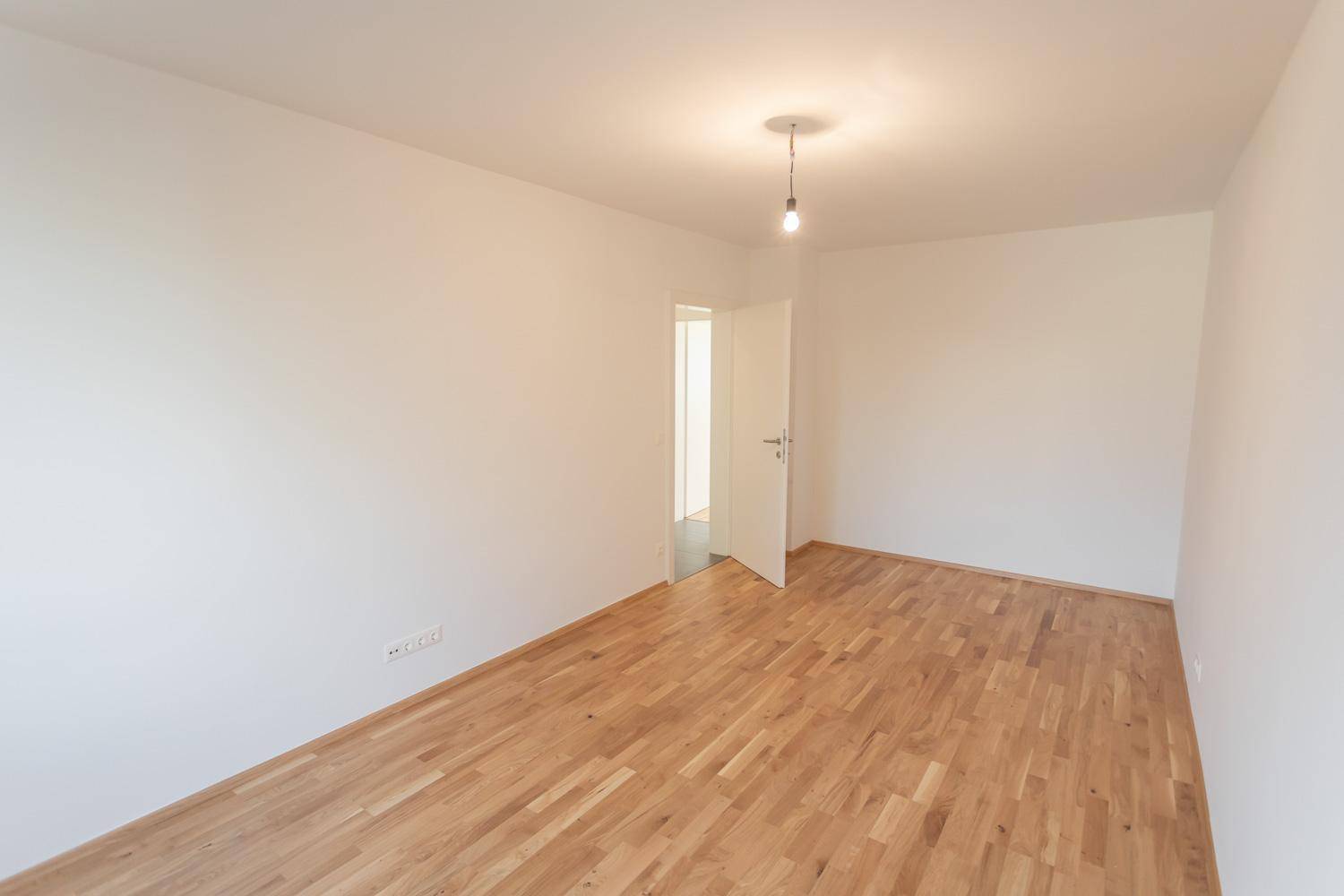 Heller, leerer Raum mit Parkettboden und Zugang zu einem weiteren Zimmer durch eine offene Tür.