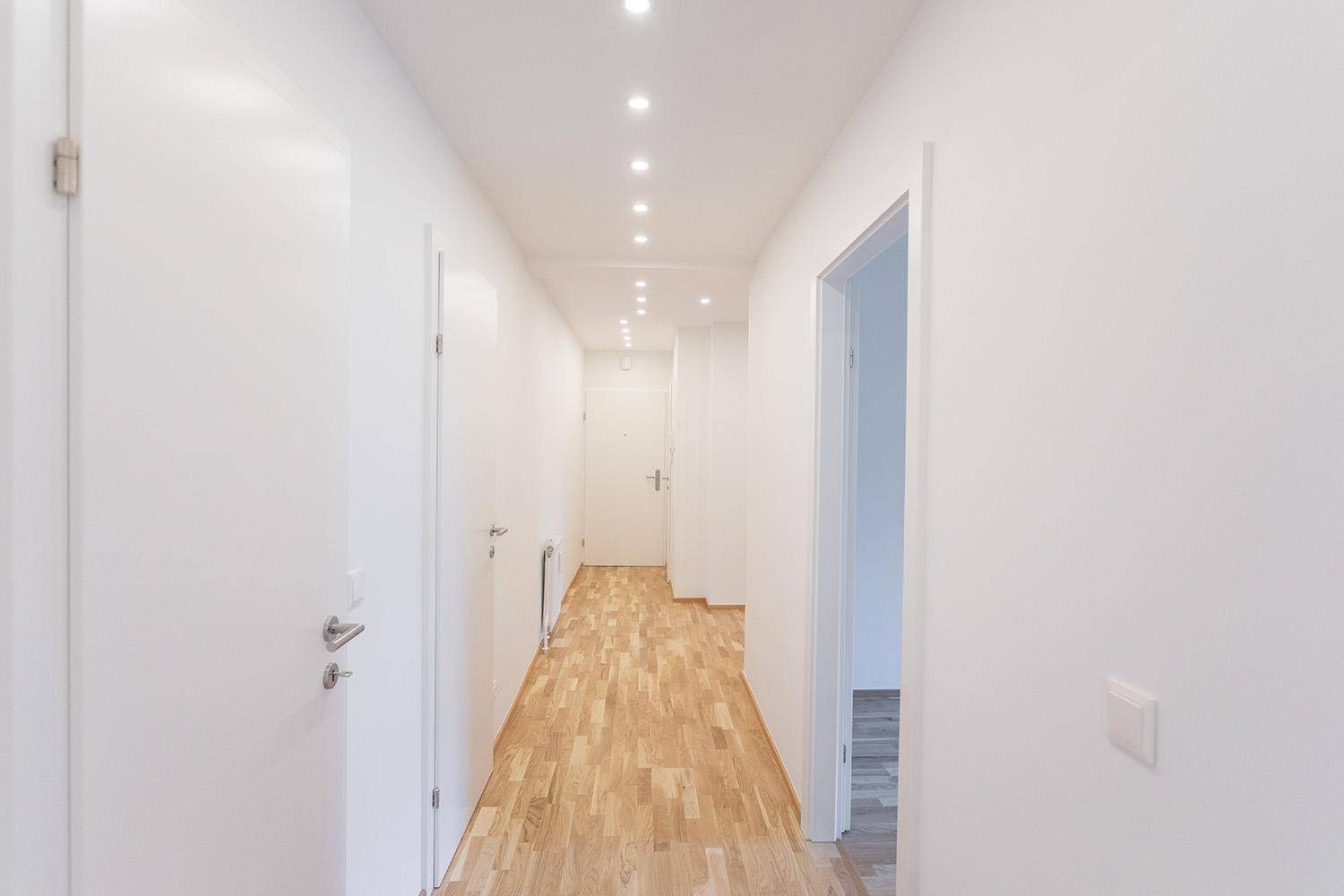 Heller Flur mit Holzboden und Einbaustrahlern, der zu weiteren Räumen der Wohnung führt.