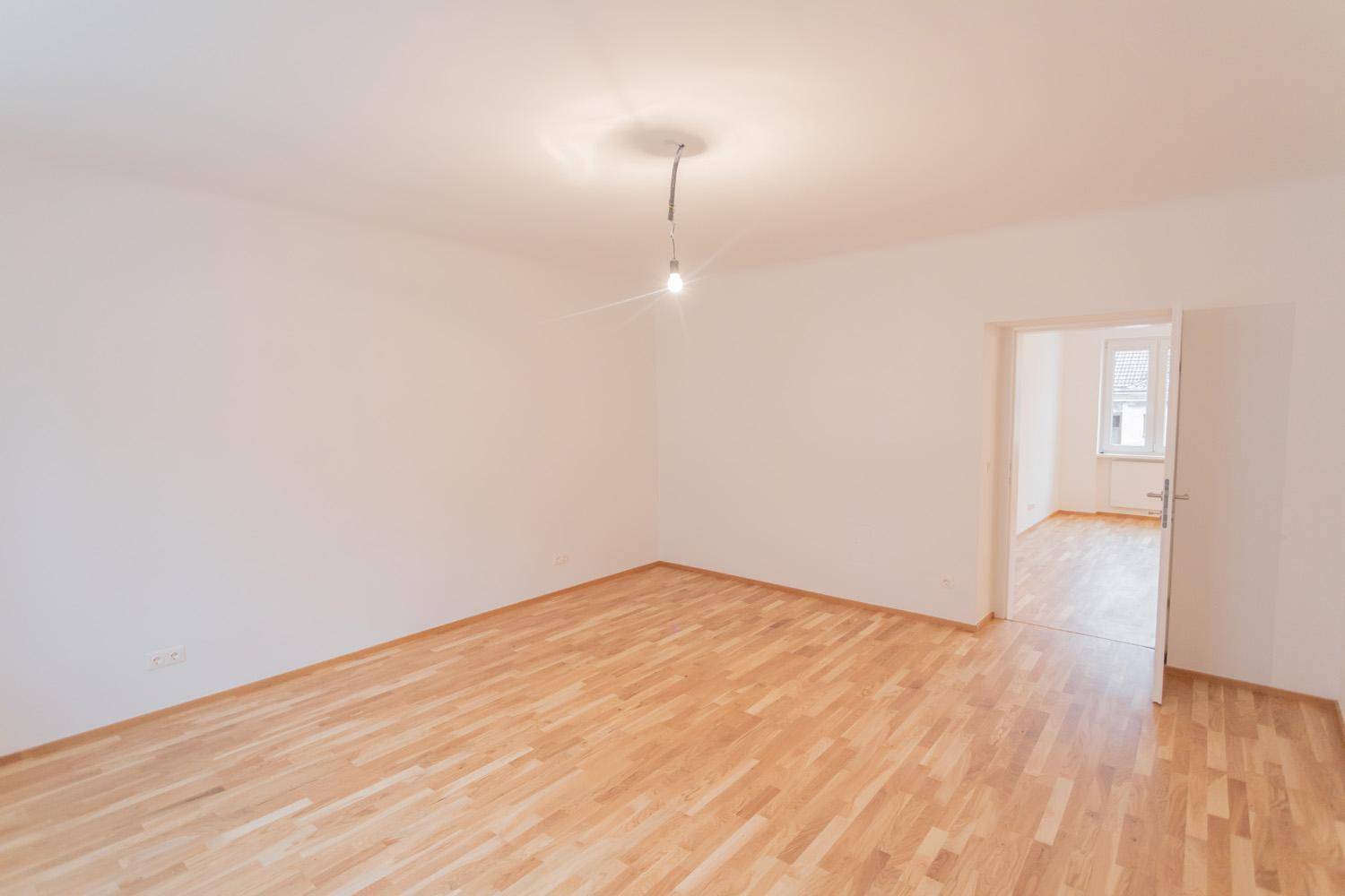 Heller Raum mit Parkettboden und Zugang zu einem weiteren Zimmer.