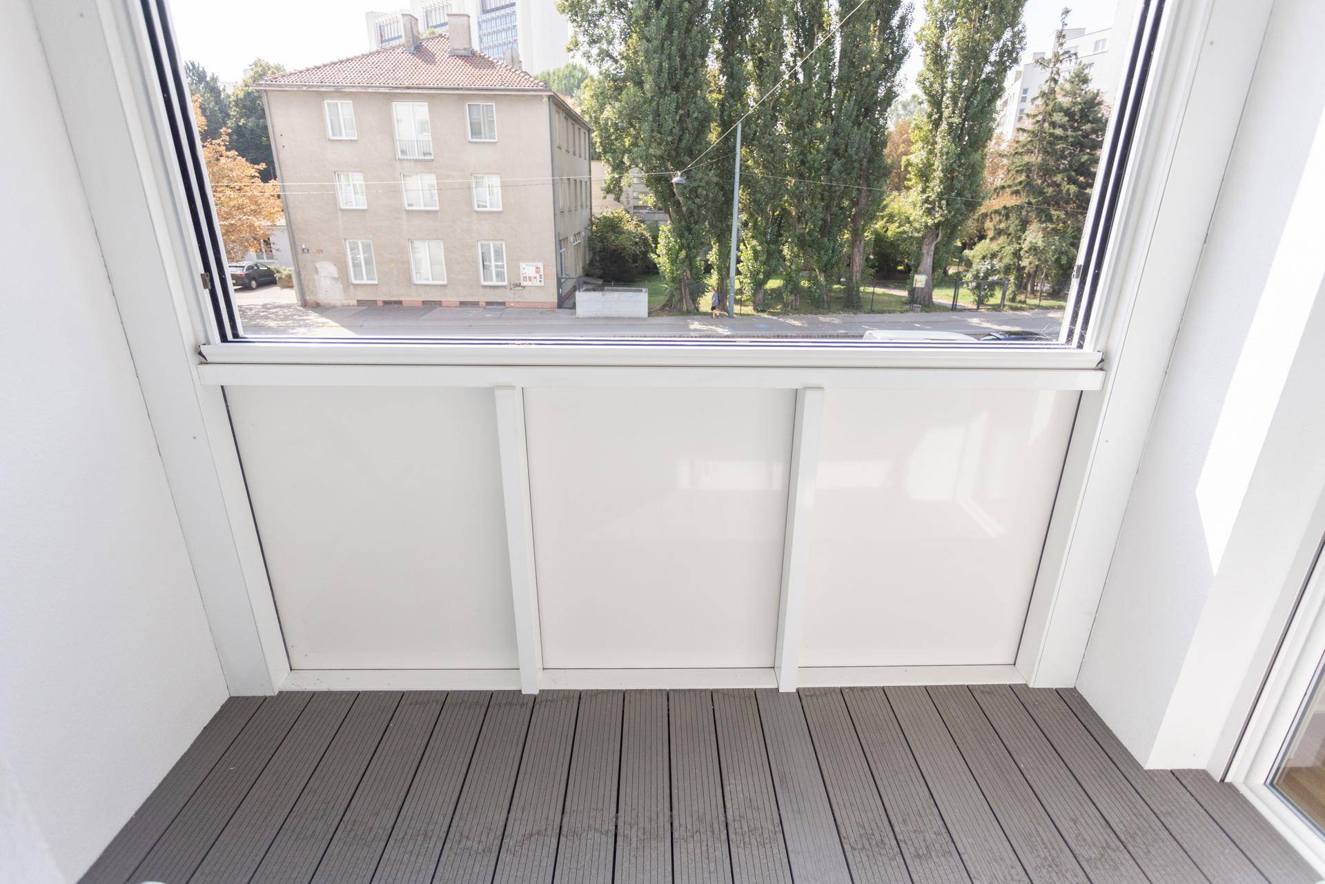 Heller Balkon mit Holzdielenboden und Blick auf die umliegende Bebauung und Bäume.